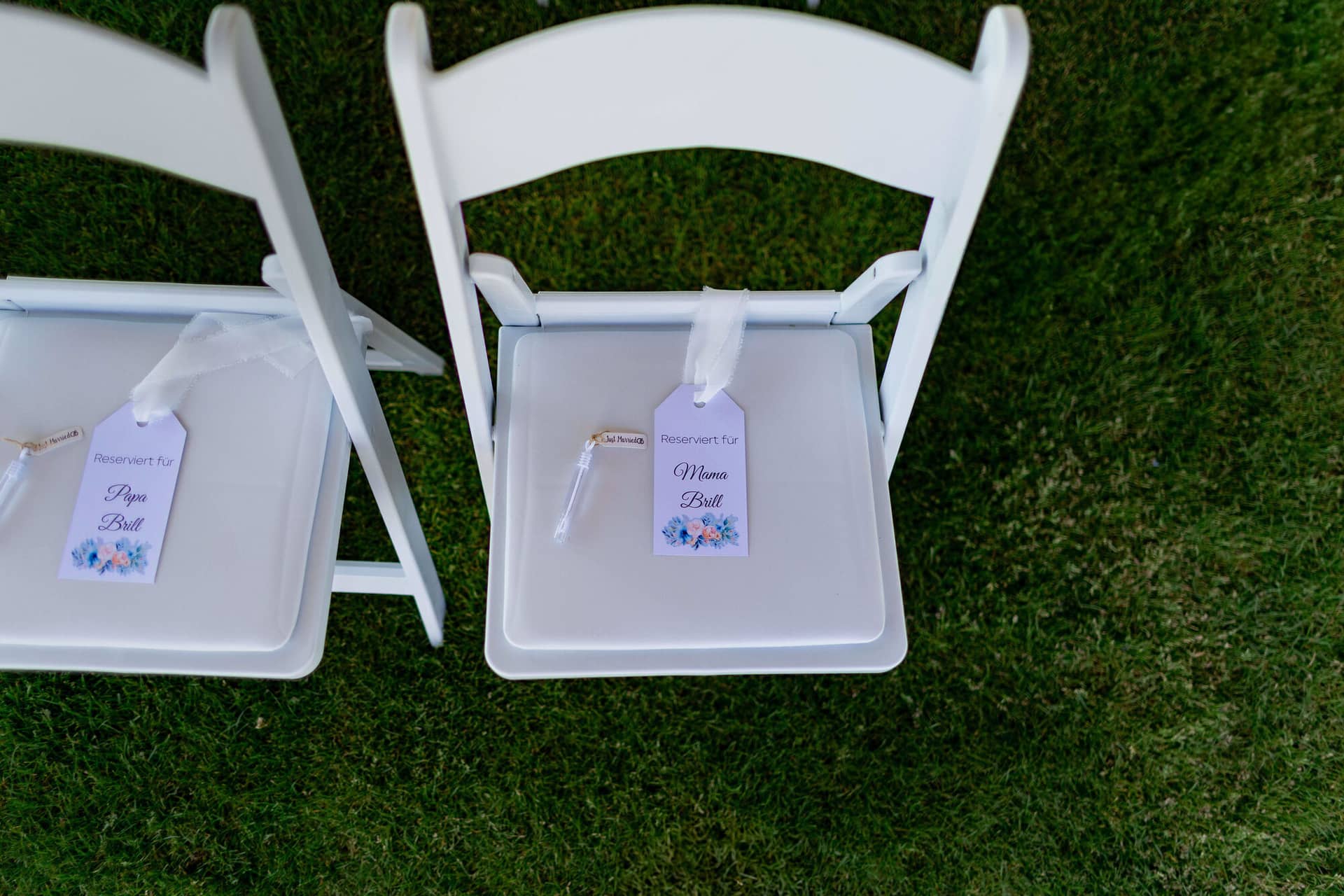 20250501 11 57 094K8A2564 Hochzeitslocation Bad Duerkheim Fritz Ritter Weingut.D6gs5WlF Personalisierte Platzkarten für Eltern auf weißen Klappstühlen im Weinberg