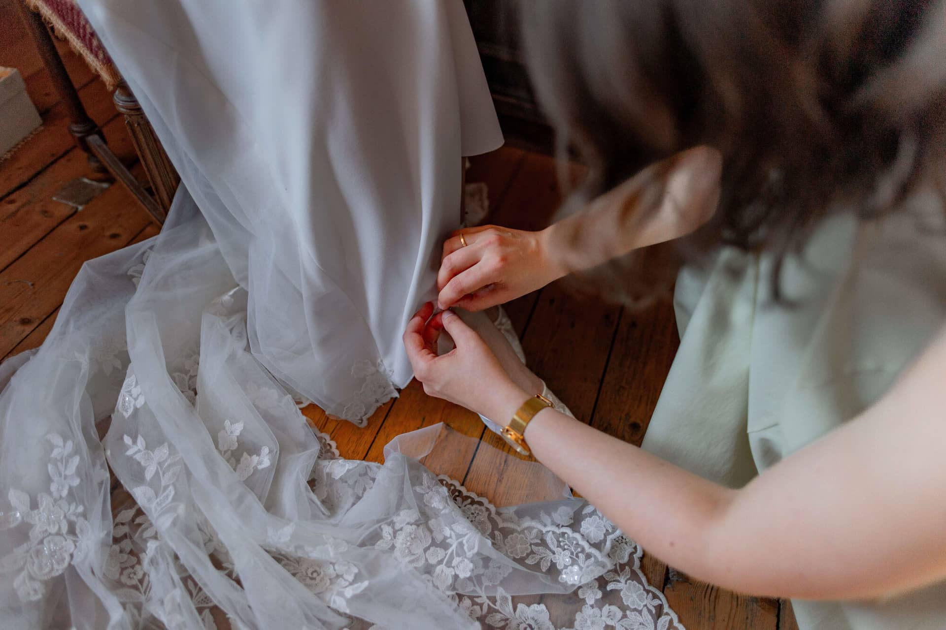 20250501 12 49 414K8A2654 Getting Ready Der Braut Im Fritz Ritter In Bad Duerkheim.B7wQlvhr Trauzeugin befestigt den Saum des Brautkleids auf dem Holzboden