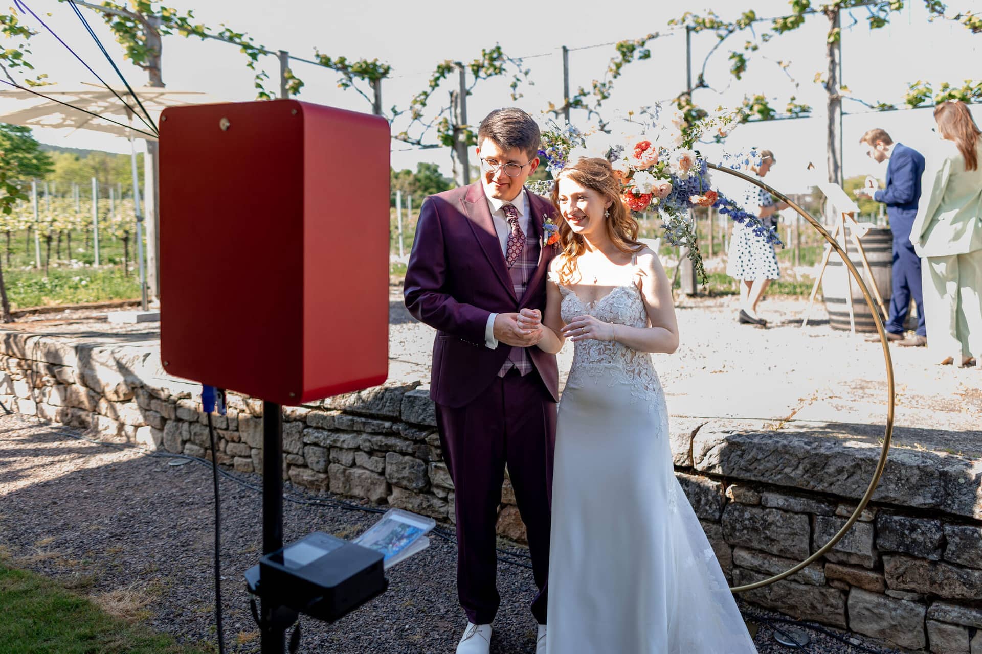 20250501 16 24 254K8A5145 Trauung Bad Duerkheim Fritz Ritter Hochzeitsfotograf.9mHrNB14 Brautpaar sitzt entspannt auf Holzbank im sonnigen Weinberg