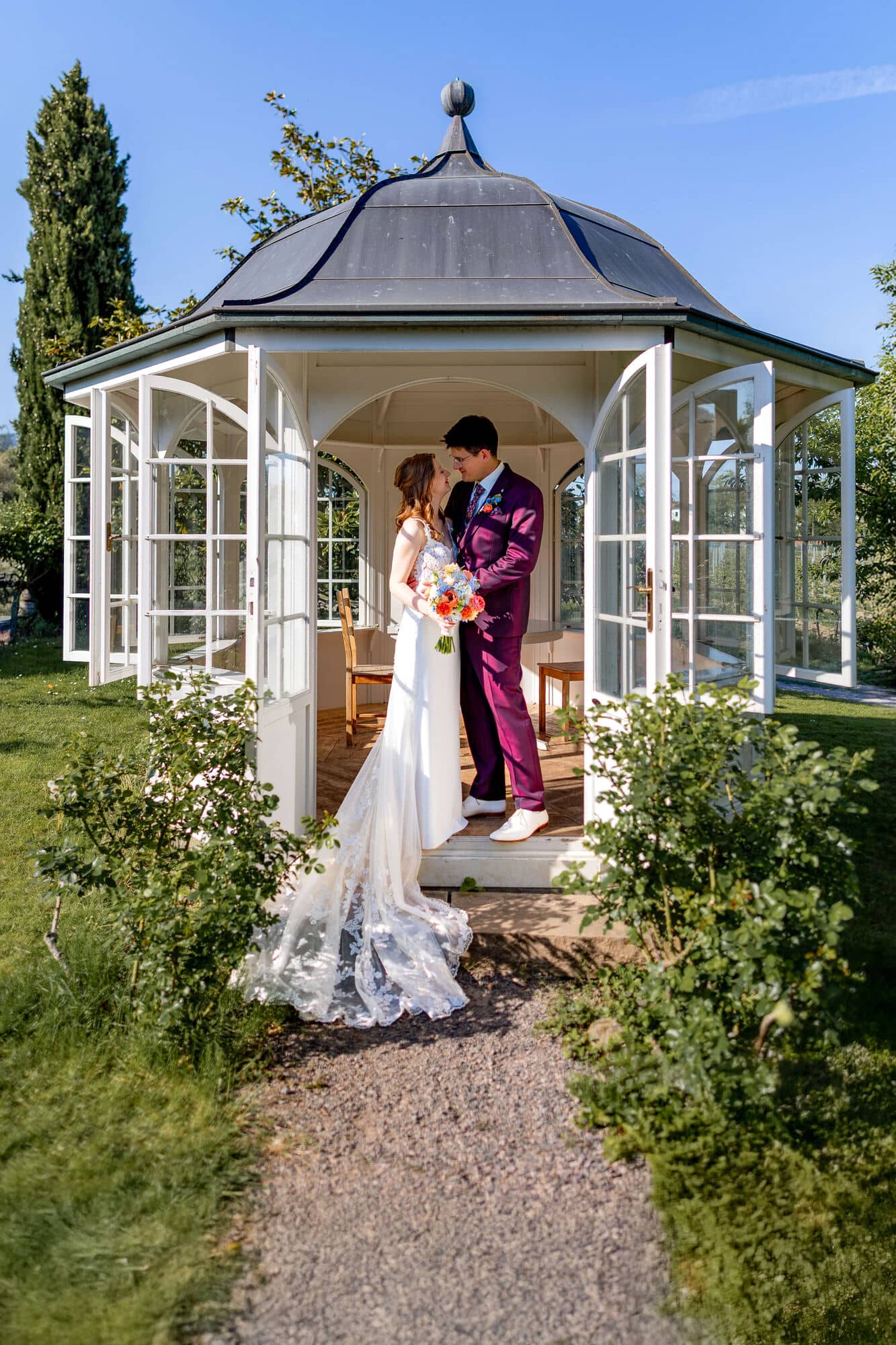 20250501 17 23 364K8A5434 Als Hochzeitsfotograf Im Fritz Ritter In Bad Duerkheim.DkwrVAdD Brautpaar von hinten auf weißer Bank sitzend mit Blick über die Weinberge Bad Dürkheims