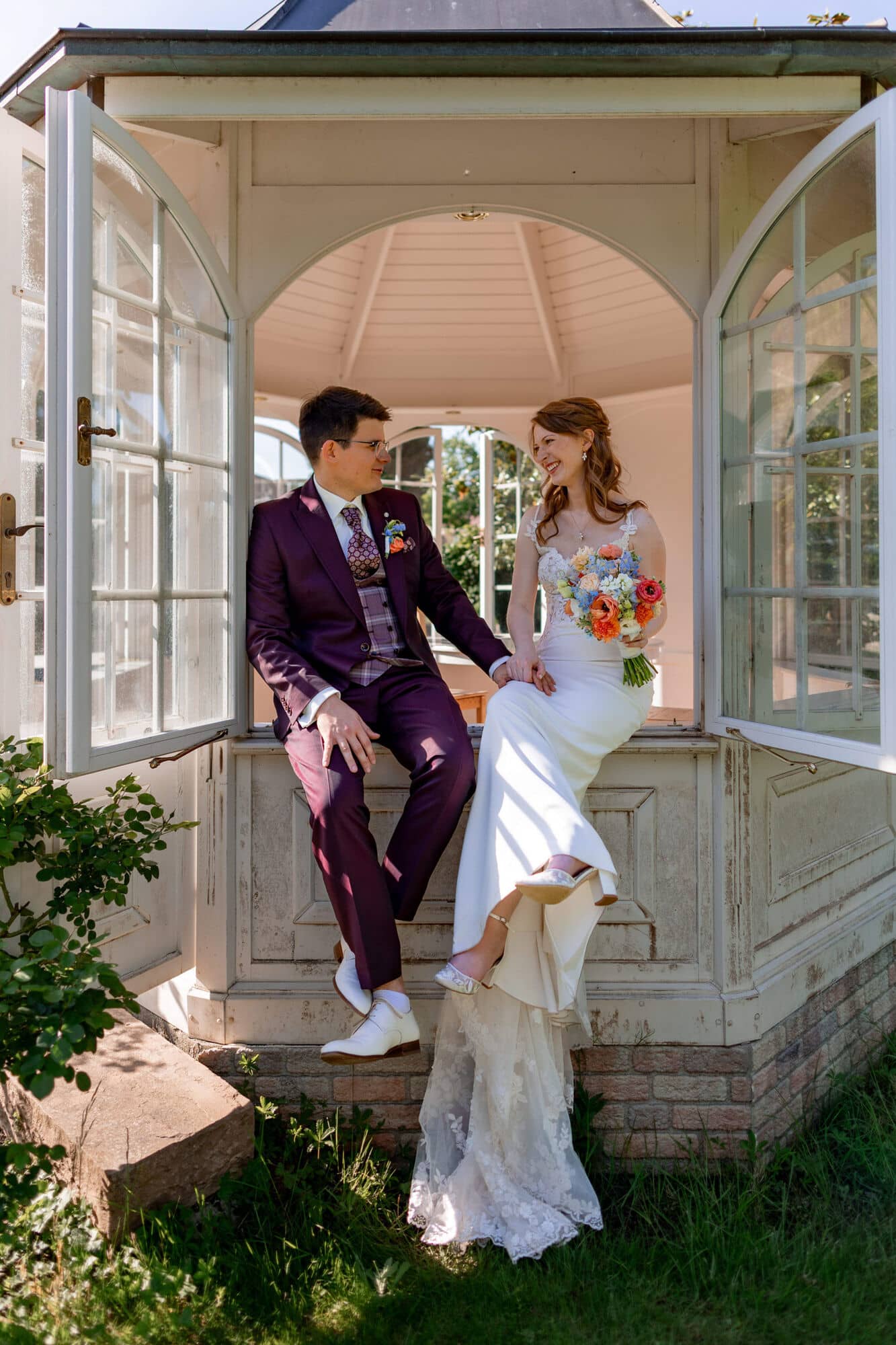 20250501 17 27 534K8A5556 Brautpaarshooting Bad Duerkheim Fritz Ritter Hochzeitsfotograf.CrFWhfix Brautpaar sitzt entspannt auf Pavillon-Bank im sonnigen Garten