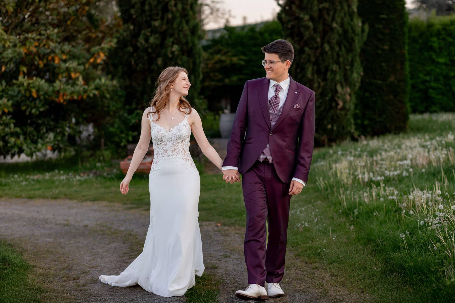 20250501 20 07 522C4A3803 Brautpaarshooting Sunnenuntergang Golden Hour Bad Duerkheim Fritz Ritter Hochzeitsfotograf.F7kiOIOH Brautpaar läuft Hand in Hand auf Kiesweg im abendlichen Gutspark