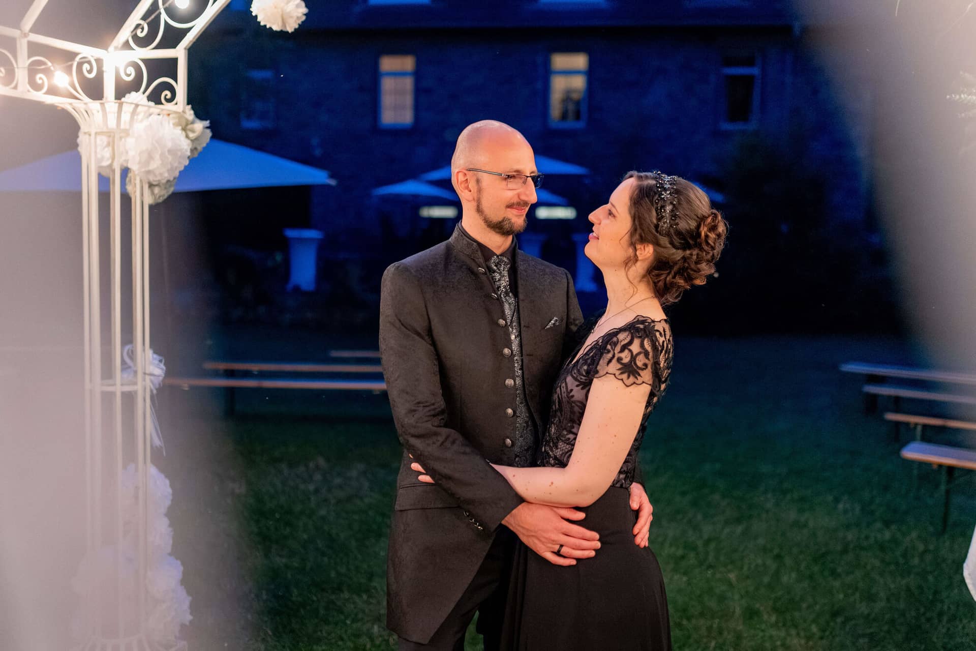 20250621 22 20 59 4K8A6934 Hochzeitsfeier Felsenmuehle Neuleinigen.DmI3Qs 0 Grün beleuchteter Innenhof mit Hochzeitstafeln und Holzstühlen