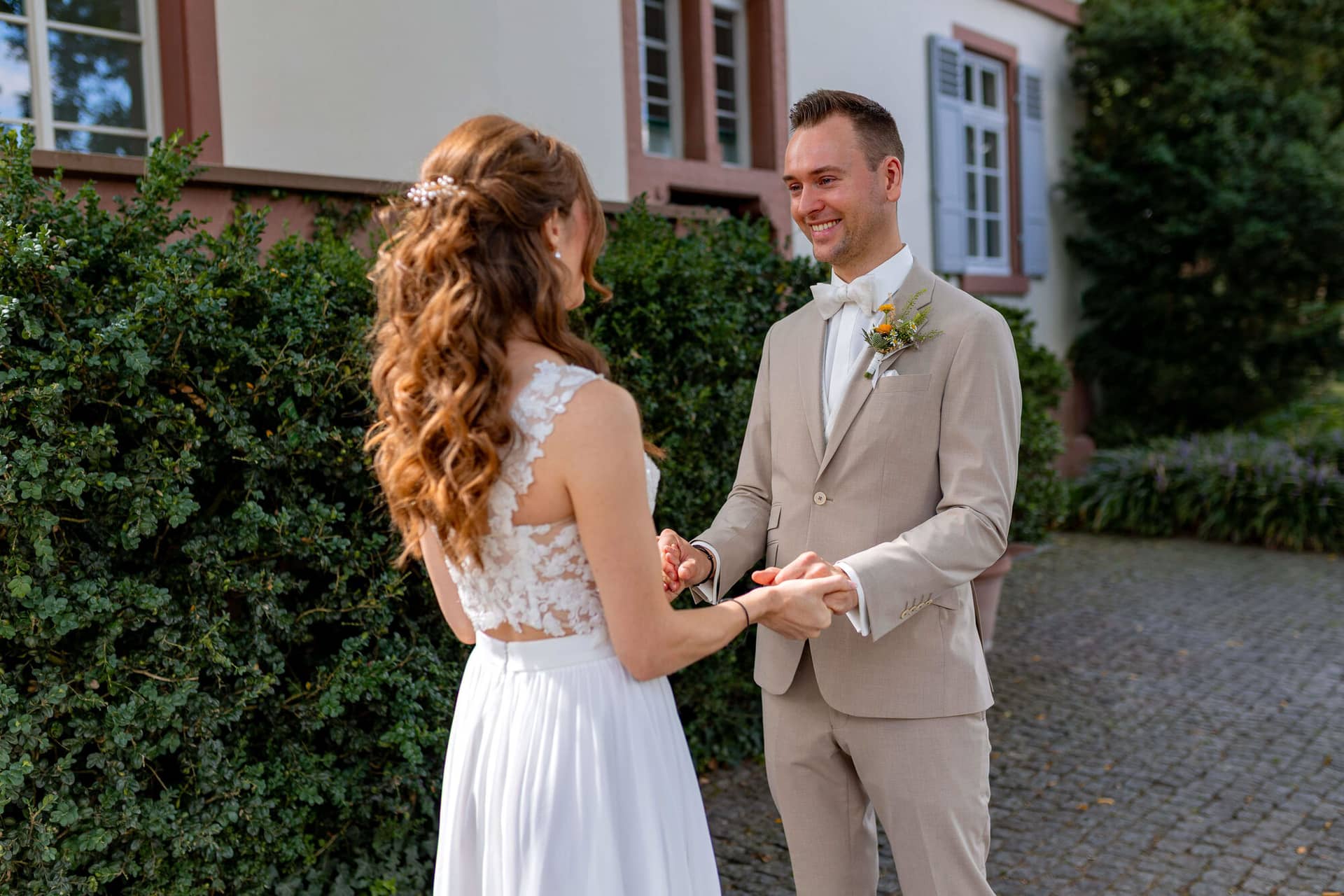 20250830 12 39 00 4K8A9838.BVIyidoC Bräutigam lächelt die Braut beim First Look an und hält ihre Hand