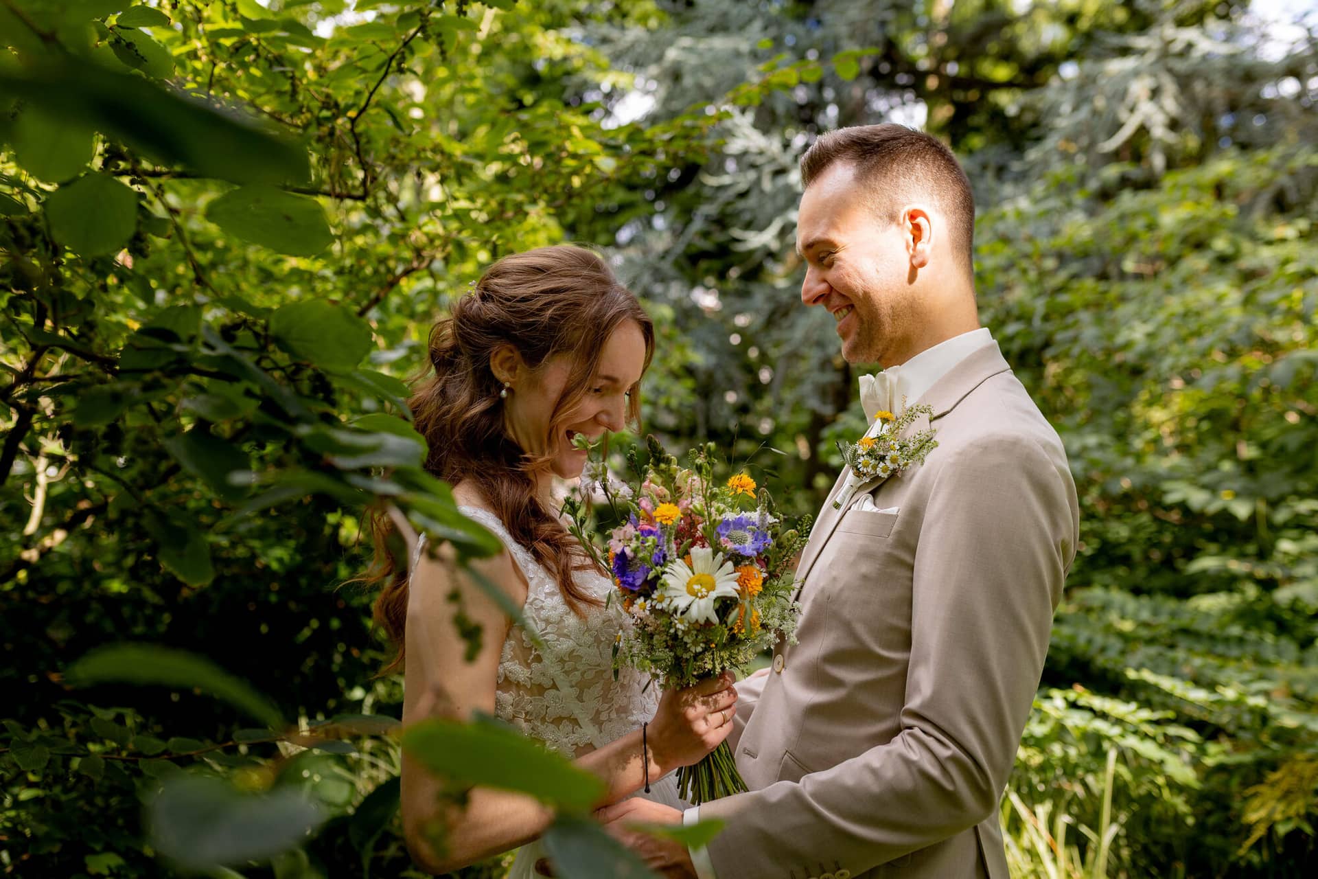 20250830 14 18 34 4K8A1204.XgXbh4DW Brautpaar lacht sich an zwischen grünem Blattwerk im Hermannshof