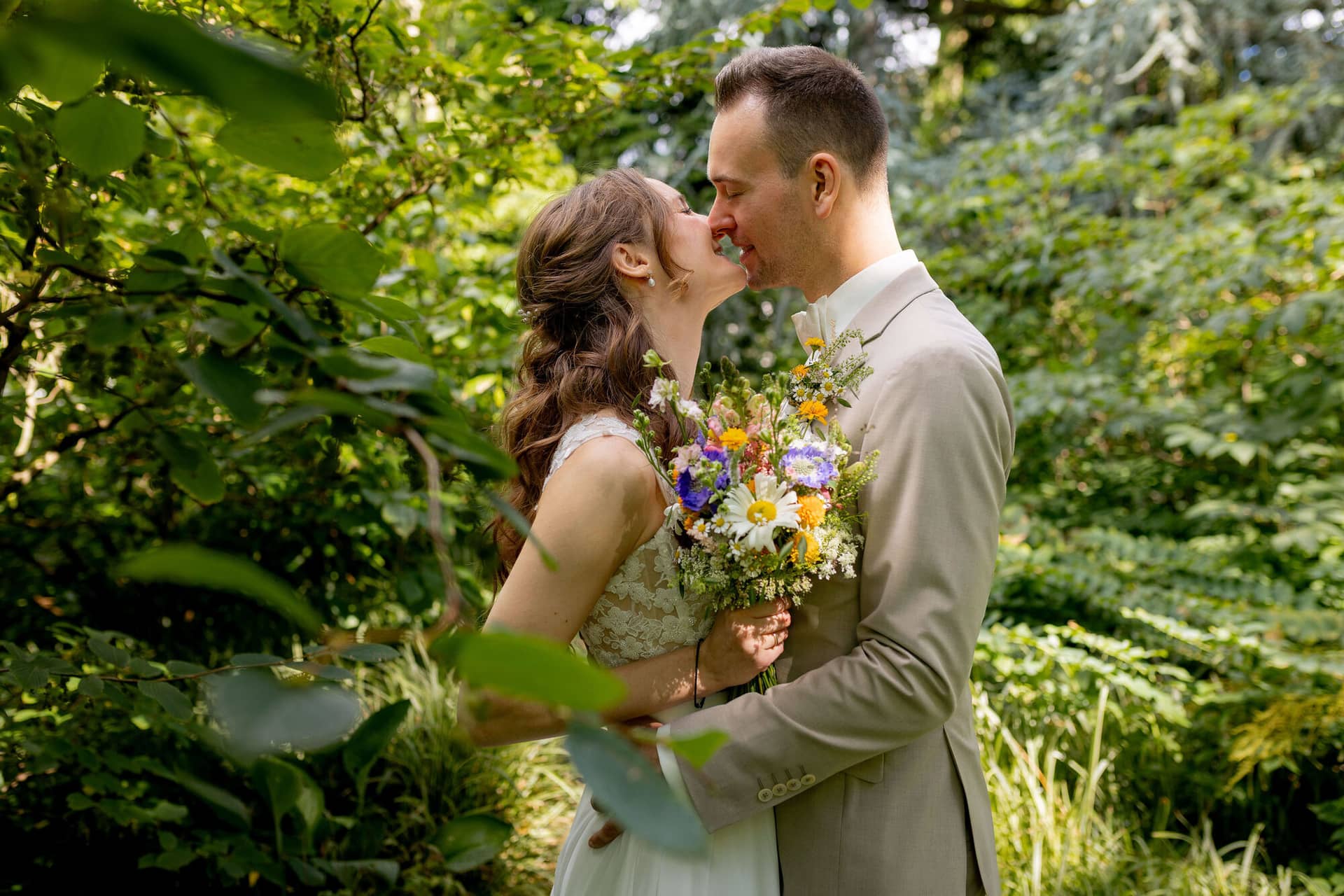 20250830 14 18 47 4K8A1245.DnhjvUps Brautpaar küsst sich umgeben von üppigem Grün im Hermannshof