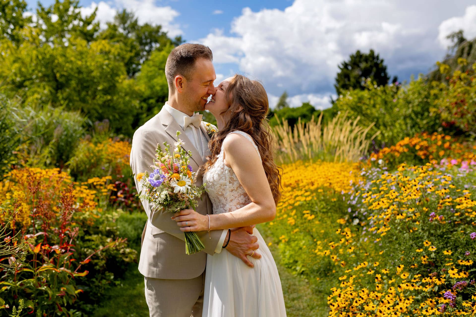 20250830 14 26 23 4K8A1360.BQZoiPOR Brautpaar küsst sich zwischen bunten Blumenbeeten im Hermannshof