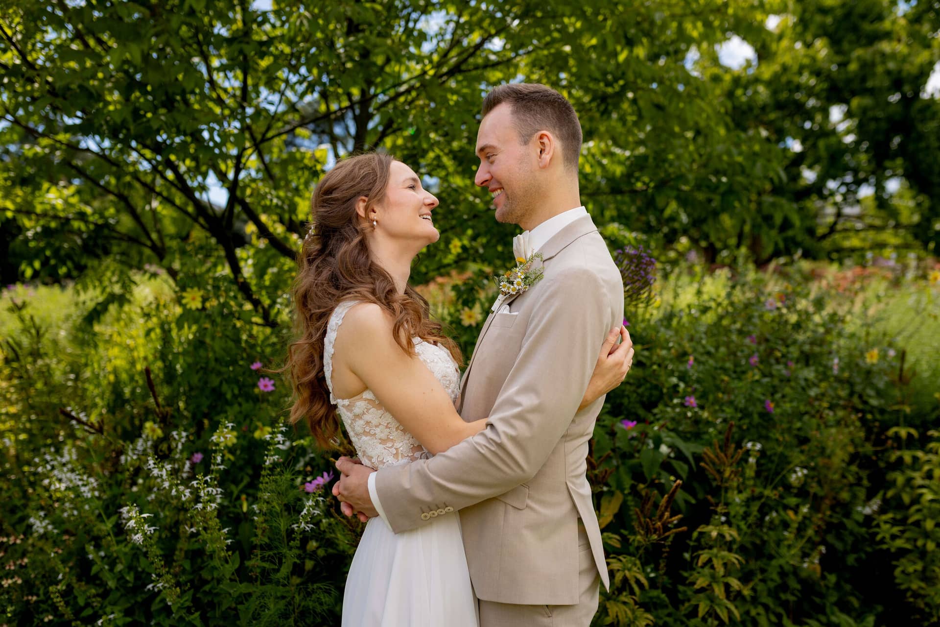 20250830 14 28 10 4K8A1433.ZCSq8eYV Brautpaar umarmt sich lächelnd vor grüner Gartenkulisse