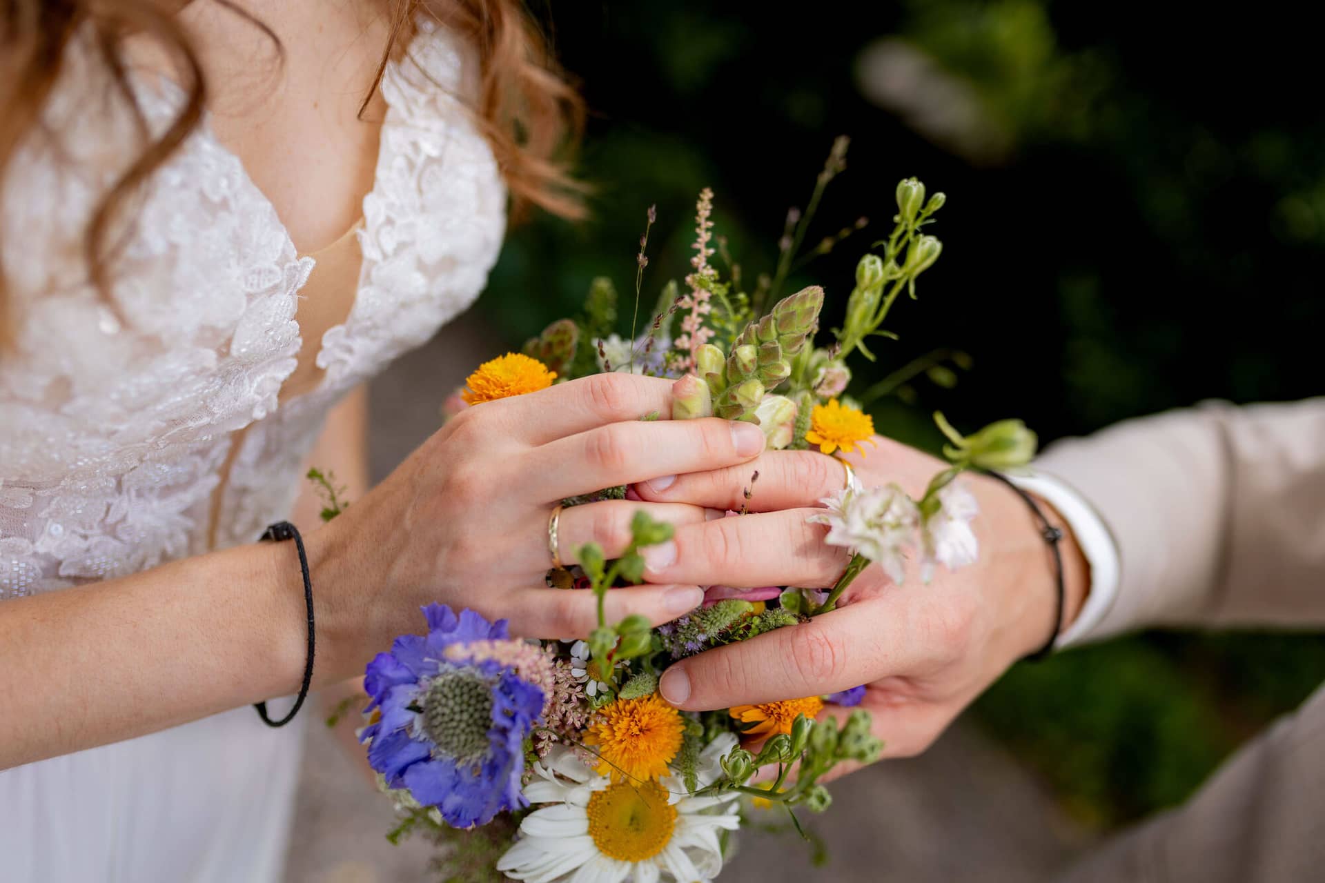 20250830 14 36 47 4K8A1490.B6oSox5k Hände des Brautpaares mit Eheringen auf dem bunten Wildblumenstrauß