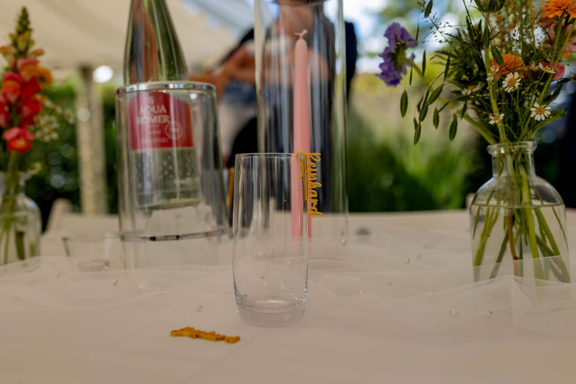 20250830 15 06 18 4K8A1574.BGKricz Trinkglas mit personalisiertem Namensschild neben Blumenvase auf dem Hochzeitstisch