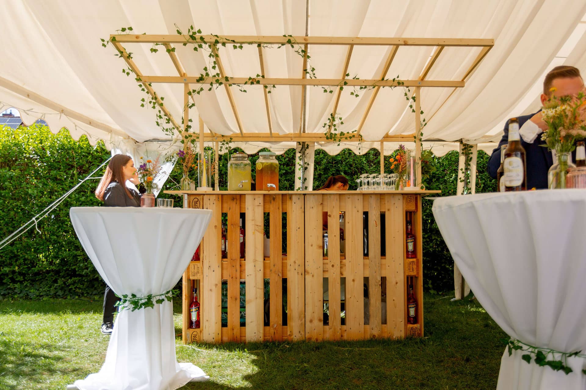 20250830 15 13 59 MK3 1119.BxgnRDPF Selbstgebaute Bar aus Holzpaletten mit Efeuranken und Stehtischen unter dem Zelt