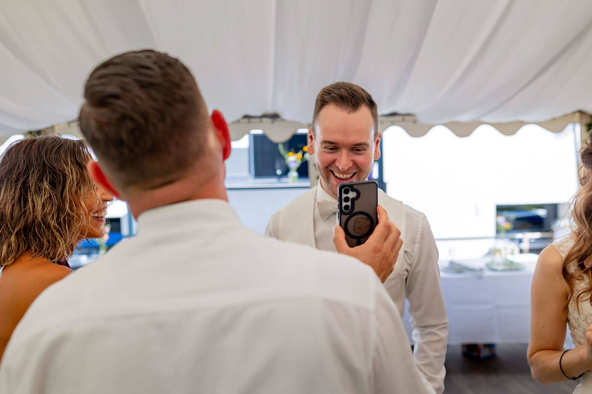 20250830 15 51 30 4K8A1867.CyoYyQ8C Bräutigam zeigt lachend ein Foto auf dem Handy bei der Gartenparty