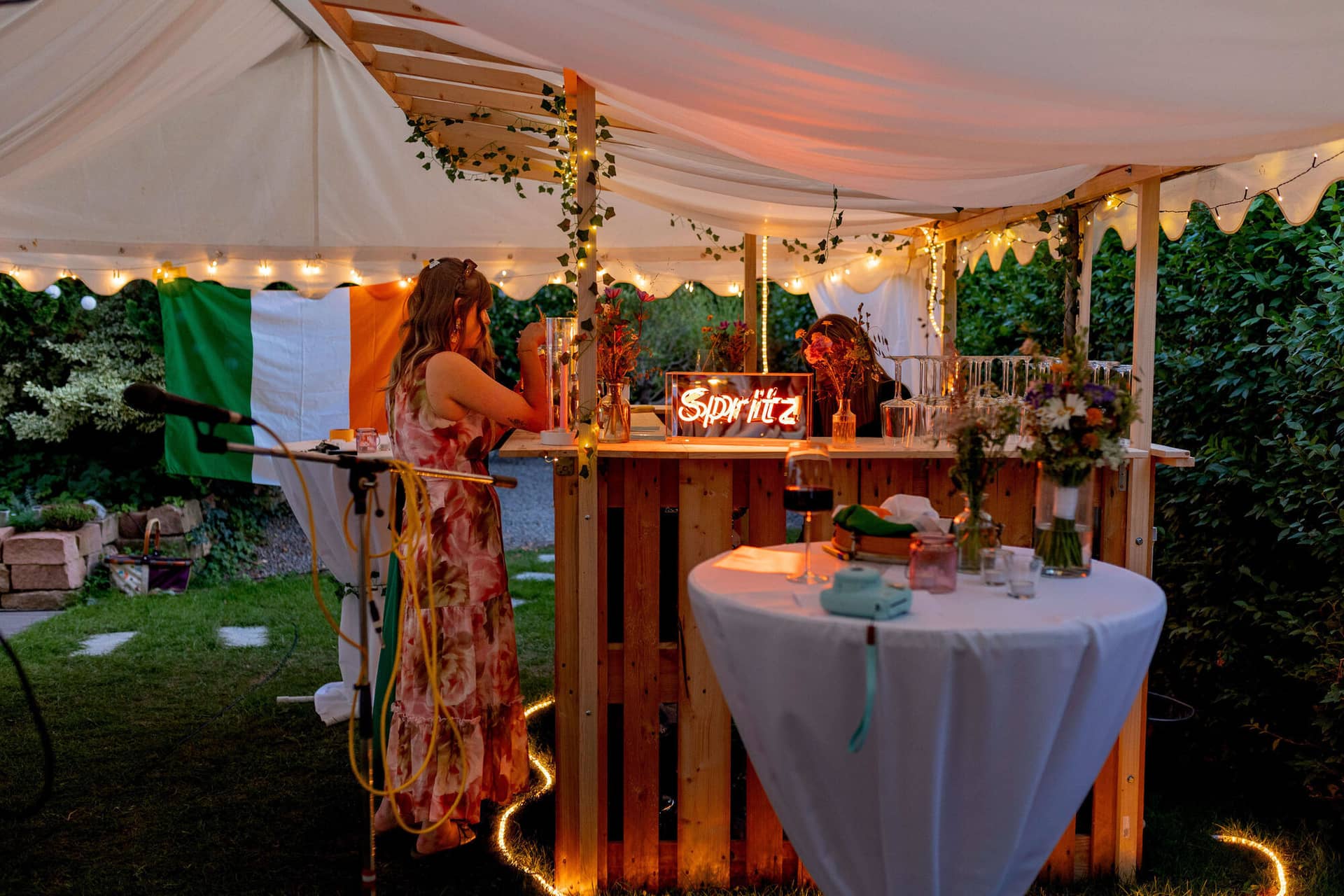 20250830 20 19 42 4K8A3430.Pbu9QaCB Beleuchtete Palettenbar mit Spritz-Neonschild und irischer Flagge am Abend