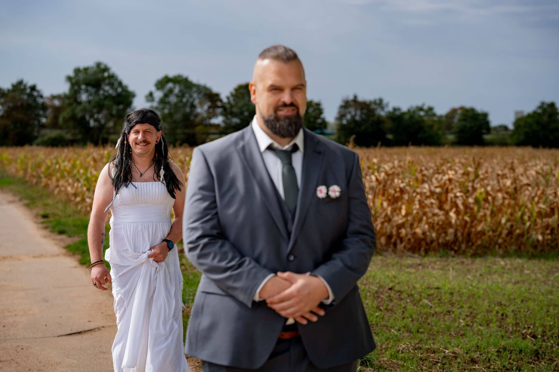 20250913 11 24 53 DSC04459.JkEXErGF Freund im weißen Kleid mit Perücke schleicht sich von hinten an den wartenden Bräutigam heran