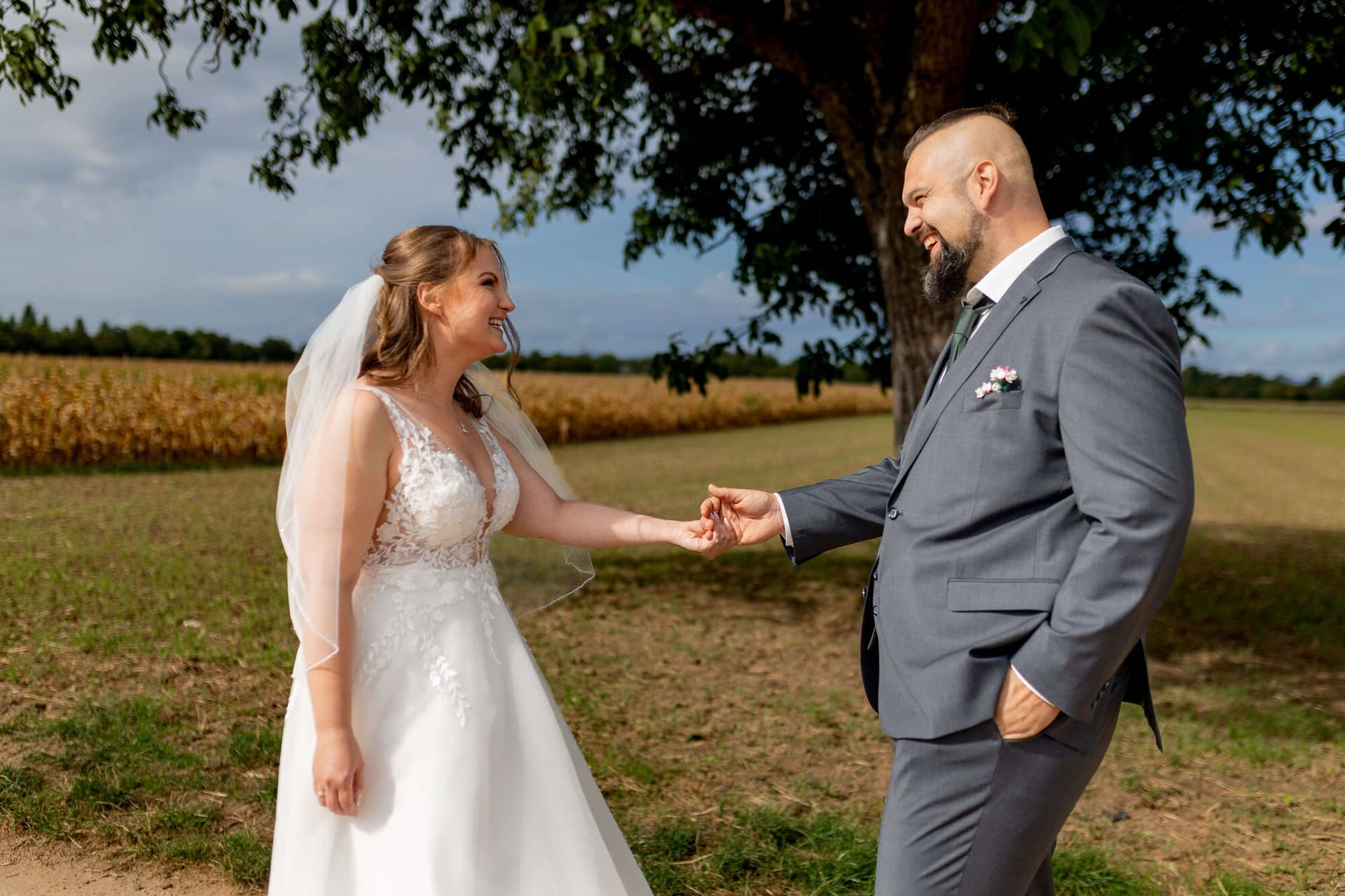 20250913 11 29 37 4K8A4193.DQLpBsNT Brautpaar hält Händchen und lächelt sich an unter einem Baum