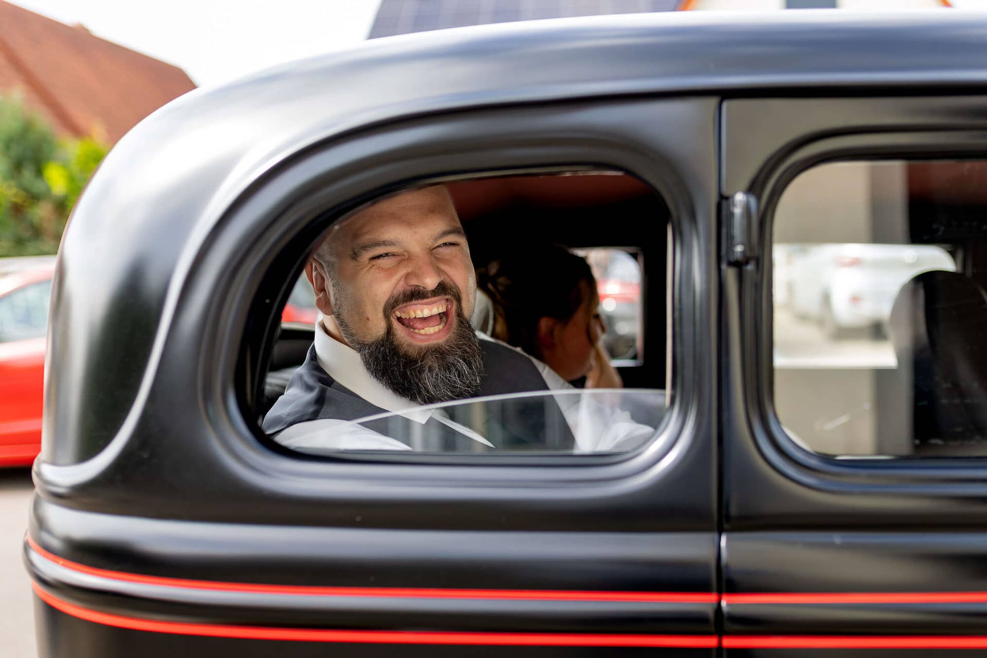 20250913 13 12 15 4K8A5529.C6PY84wo Bräutigam lacht aus dem Fenster des schwarzen Oldtimers