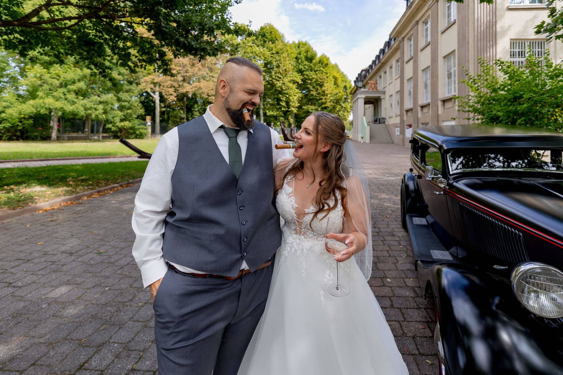 20250913 14 10 36 4K8A5953.5QrGALCV Brautpaar geht lachend neben dem schwarzen Oldtimer