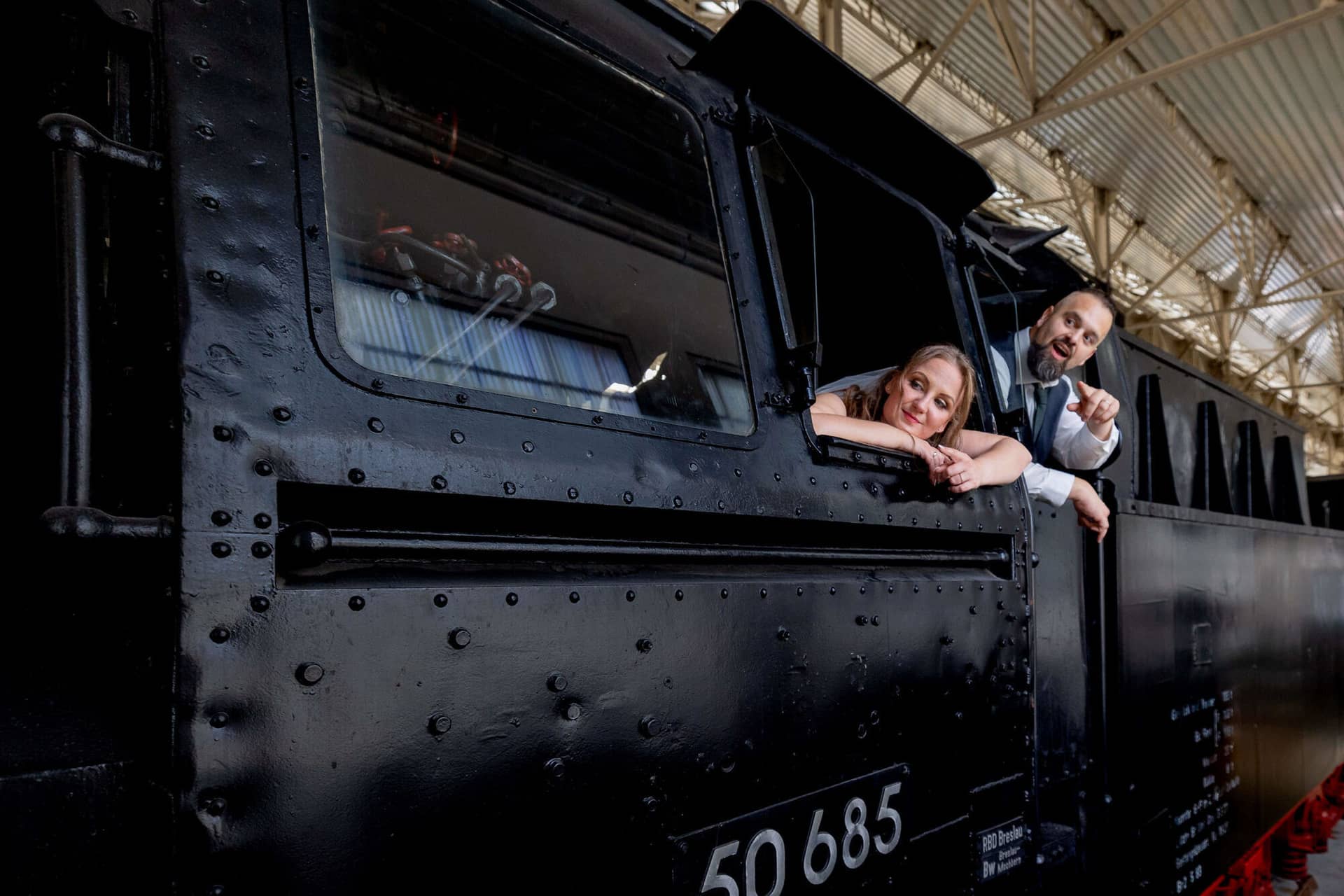 20250913 15 20 12 4K8A6616.WzszNRqc Brautpaar lehnt sich aus der Dampflok und lächelt in die Kamera