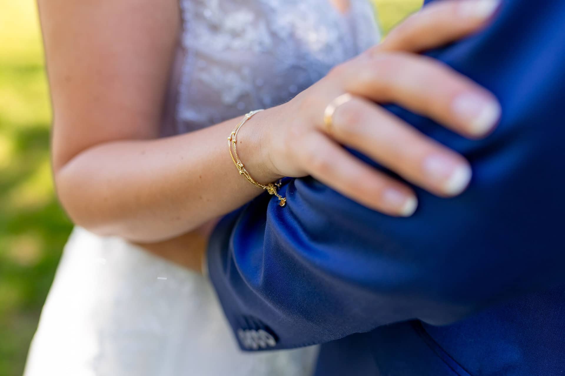 4K8A0565 Hochzeitsfotograf Mutterstadt Grenzhof Heidelberg .DqBOwIHc Nahaufnahme der Hand der Braut mit goldenem Ehering und Armband, Bräutigam hält das blaue Jackett