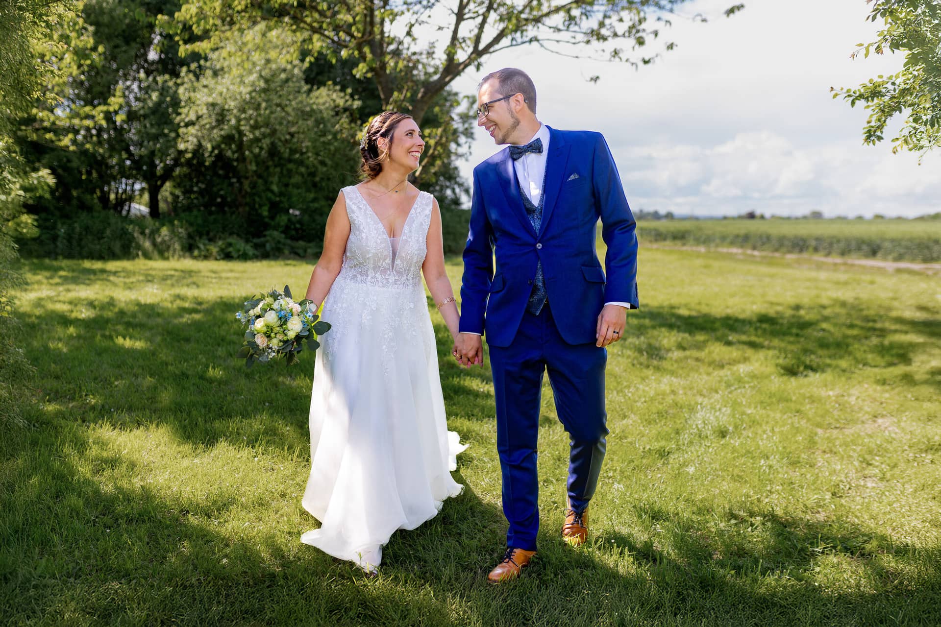 4K8A0693 Bearbeitet Bearbeitet Hochzeitsfotograf Mutterstadt Grenzhof Heidelberg .CimKXV7g Braut und Bräutigam laufen Hand in Hand durch eine grüne Sommerwiese im goldenen Sonnenlicht beim Grenzhof