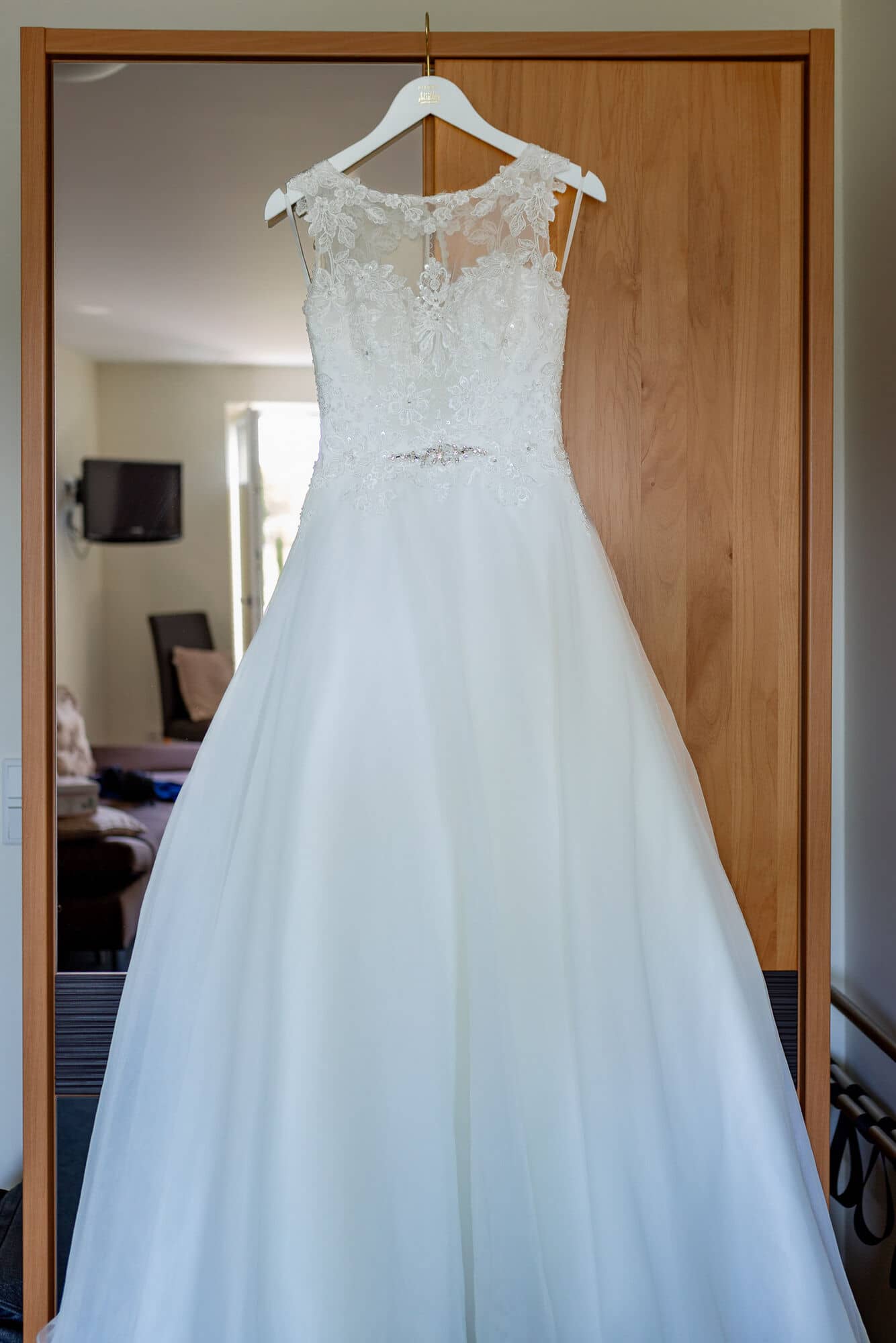 Anne Christian Hochzeitsfotograf Birkenheide Grosskarlbach Bissersheim 00001.CwBWjyLn Weißes, glitzerndes Hochzeitskleid mit Volants und Spitze hängt an einem Schirm vor altem Holztor