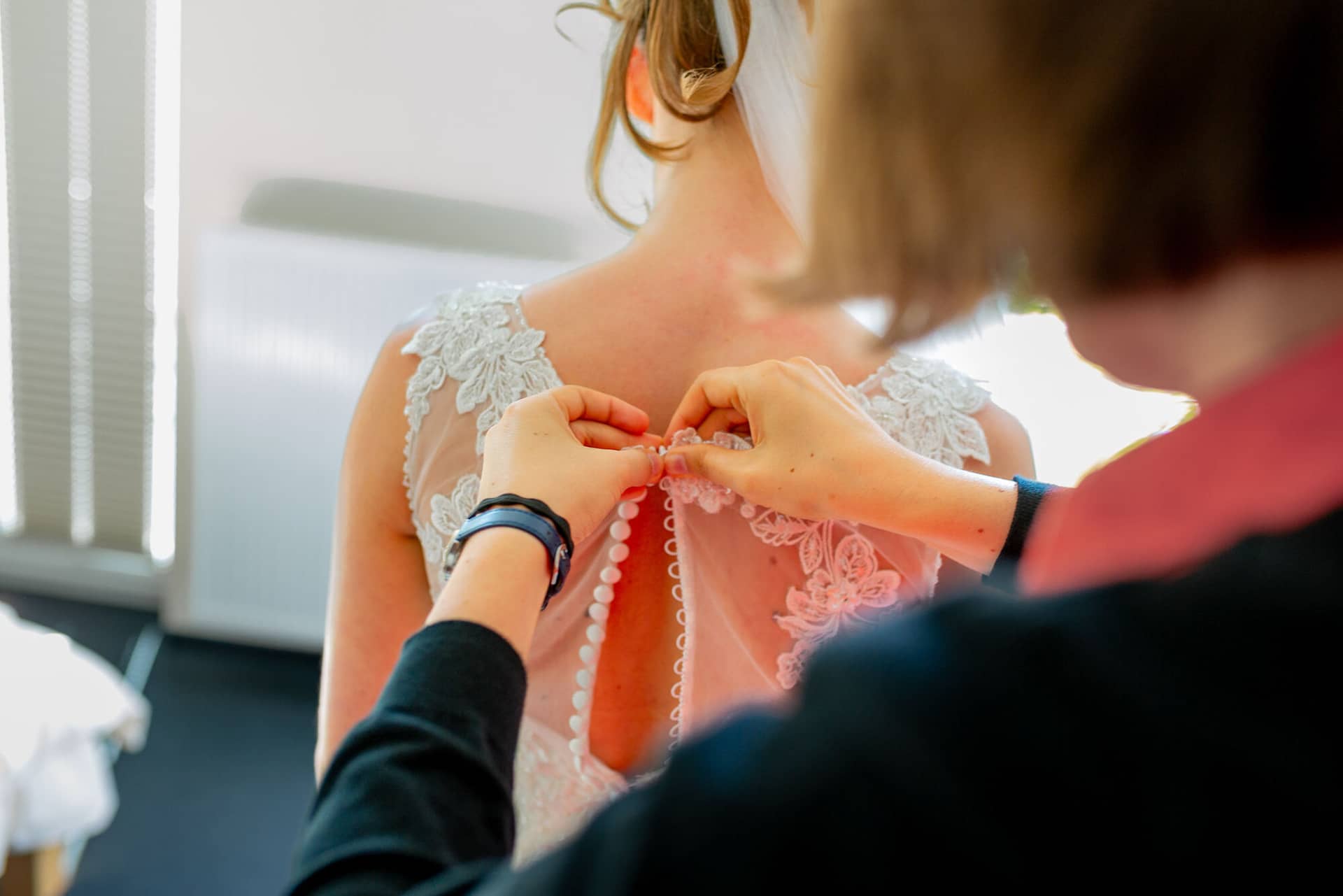 Anne Christian Hochzeitsfotograf Birkenheide Grosskarlbach Bissersheim 00002.JIC47Vjo Hand befestigt zart weiße Perlen am Rücken des hochgesteckten, blumengeschmückten Brautkleides