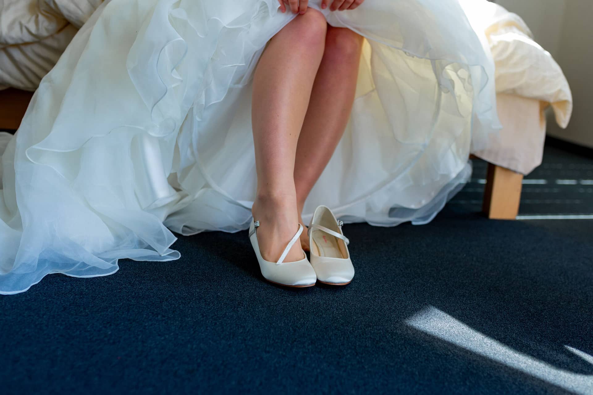 Anne Christian Hochzeitsfotograf Birkenheide Grosskarlbach Bissersheim 00004.BVKeM 17 Braut sitzt auf dem Bett und zieht weiße Paillettenballerinas mit Schleife an