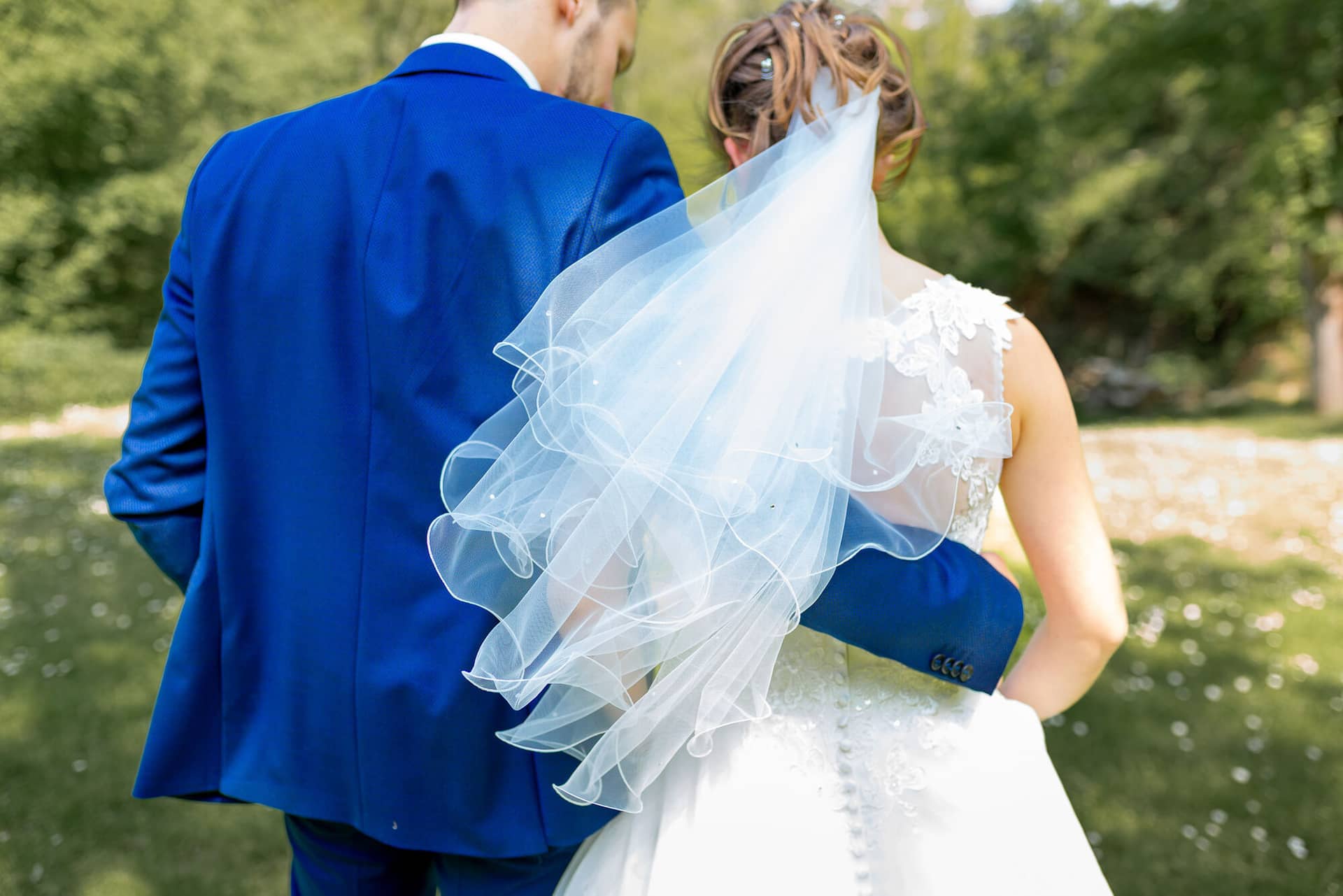 Anne Christian Hochzeitsfotograf Birkenheide Grosskarlbach Bissersheim 00008.PLl2GA7C Brautpaar im Outdoor-Shooting, Bräutigam hält liebevoll den Schleier seiner Braut im Gegenlicht