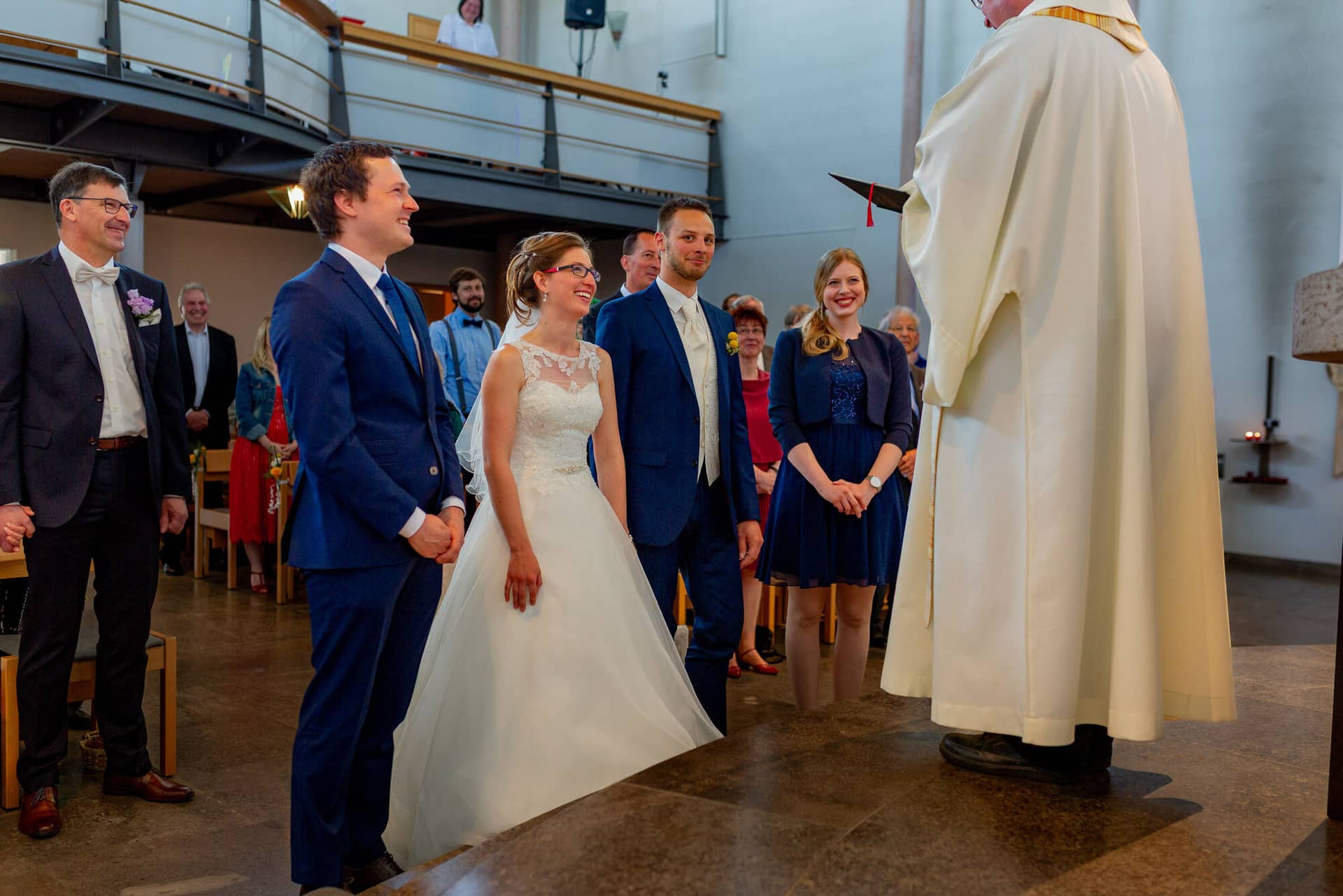 Anne Christian Hochzeitsfotograf Birkenheide Grosskarlbach Bissersheim 00010.BIDhWCJs Brautpaar und Trauzeugen lauschen dem Priester während der kirchlichen Trauung im Kirchenschiff