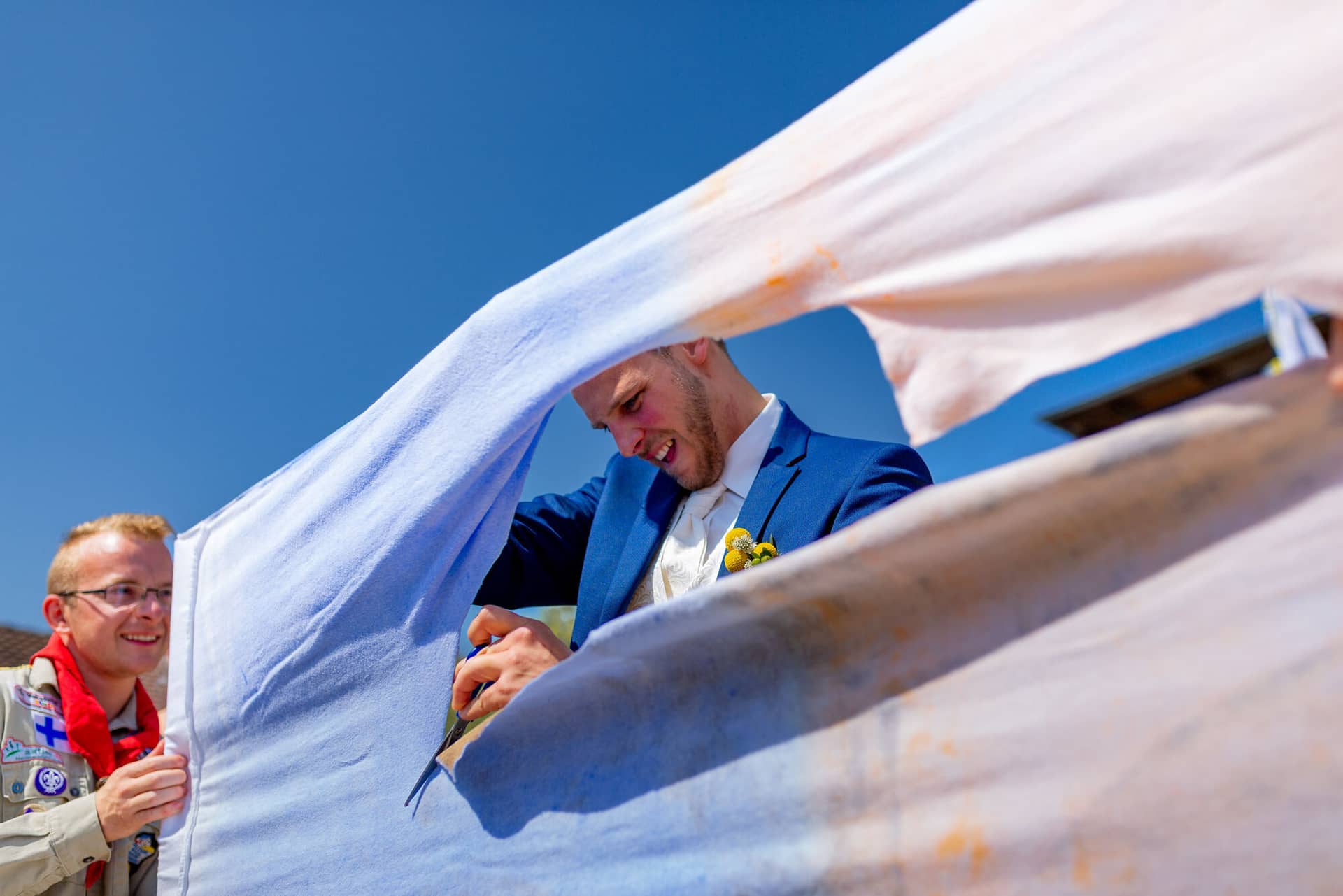 Anne Christian Hochzeitsfotograf Birkenheide Grosskarlbach Bissersheim 00014.CekZir7z Brautpaar steht unter weißem Tuch im Freien, Trauzeugen und Gäste rahmen das Paar bei strahlendem Sonnenschein ein