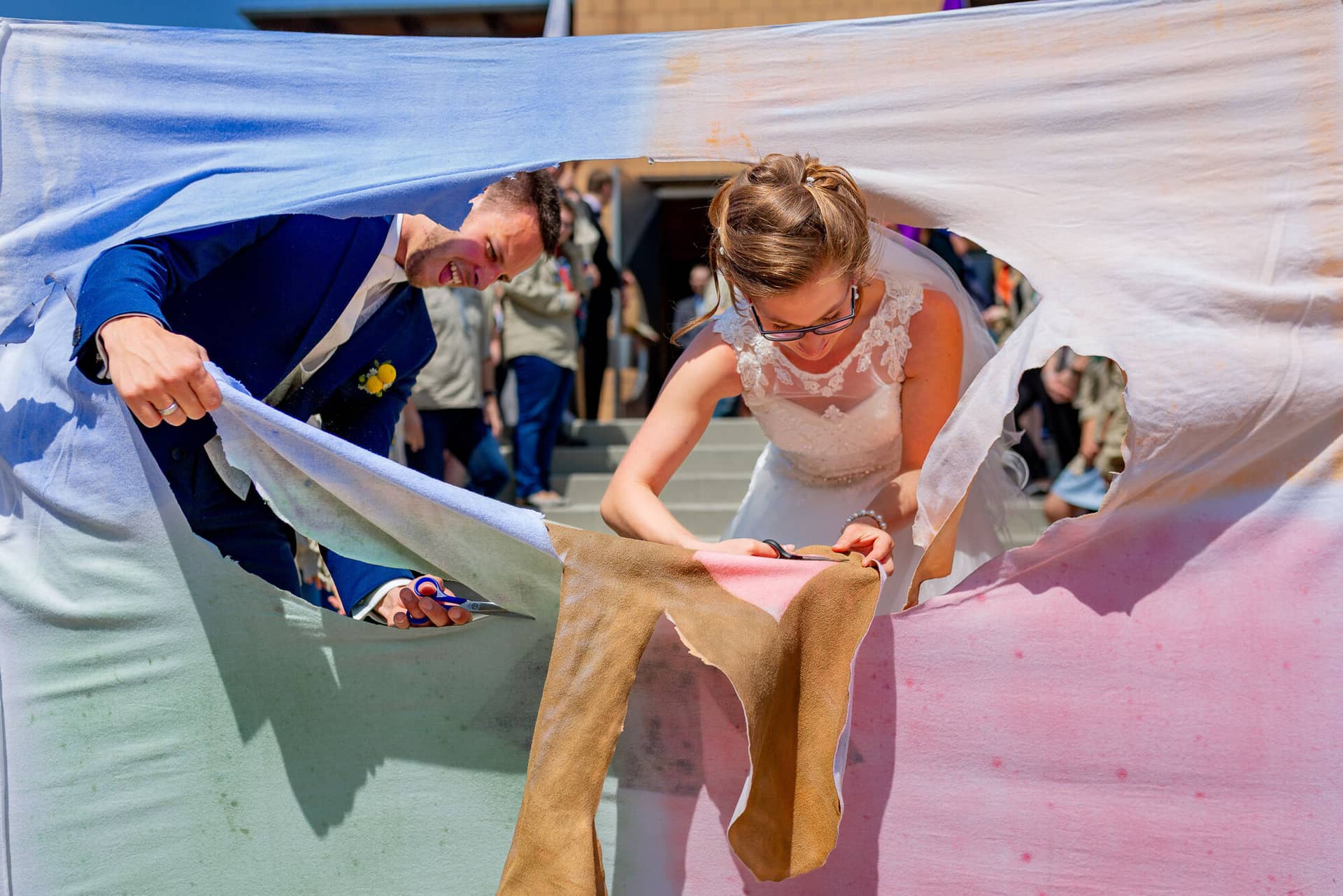 Anne Christian Hochzeitsfotograf Birkenheide Grosskarlbach Bissersheim 00015.CLL7nTnr Braut und Gast schneiden gemeinsam ein rosa und lila Stofftuch als Hochzeitsritual unter freiem Himmel