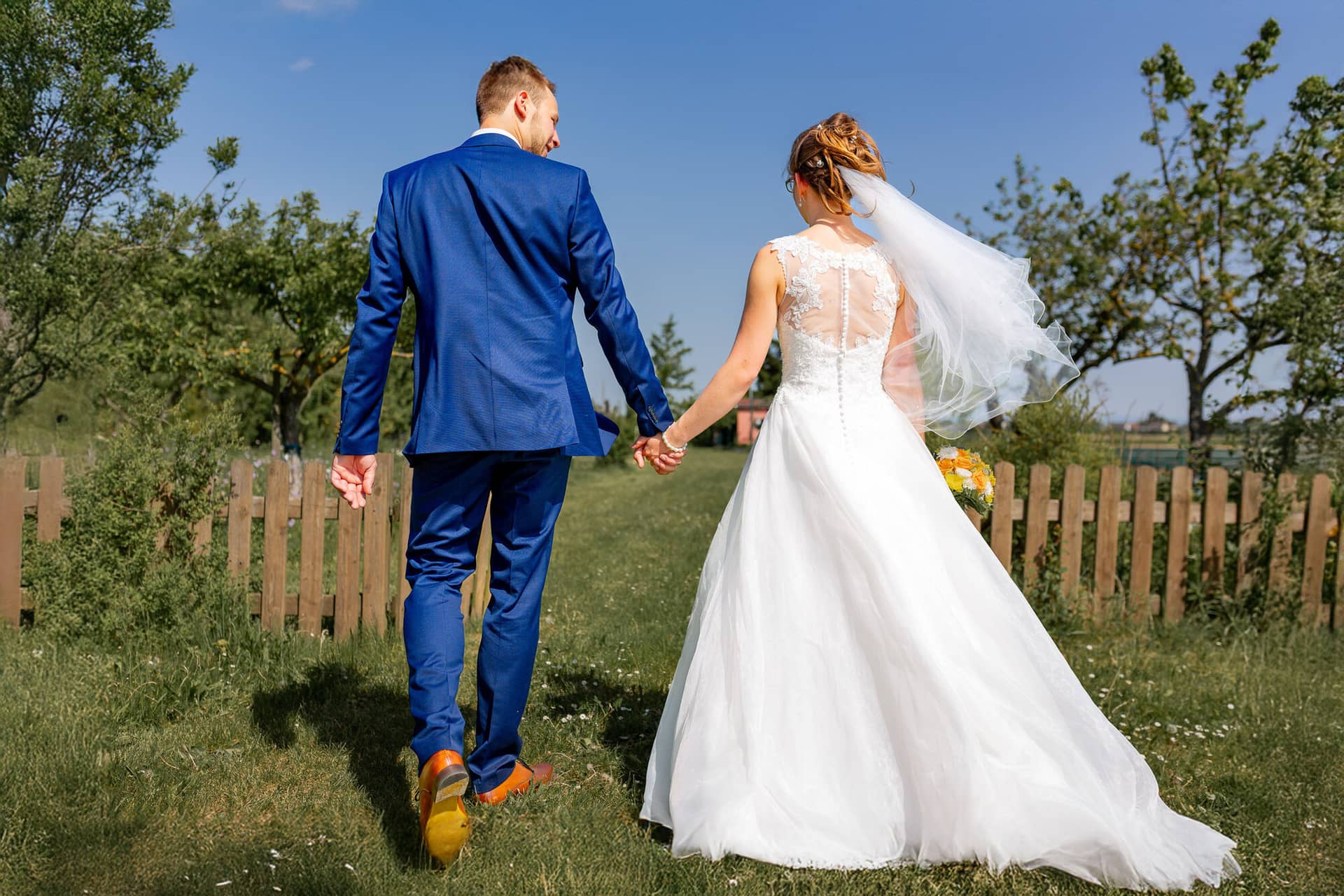 Anne Christian Hochzeitsfotograf Birkenheide Grosskarlbach Bissersheim 00019.BAQBhTaZ Brautpaar hält Hände und spaziert gemeinsam auf einem Weg, Braut im weißen Hochzeitskleid