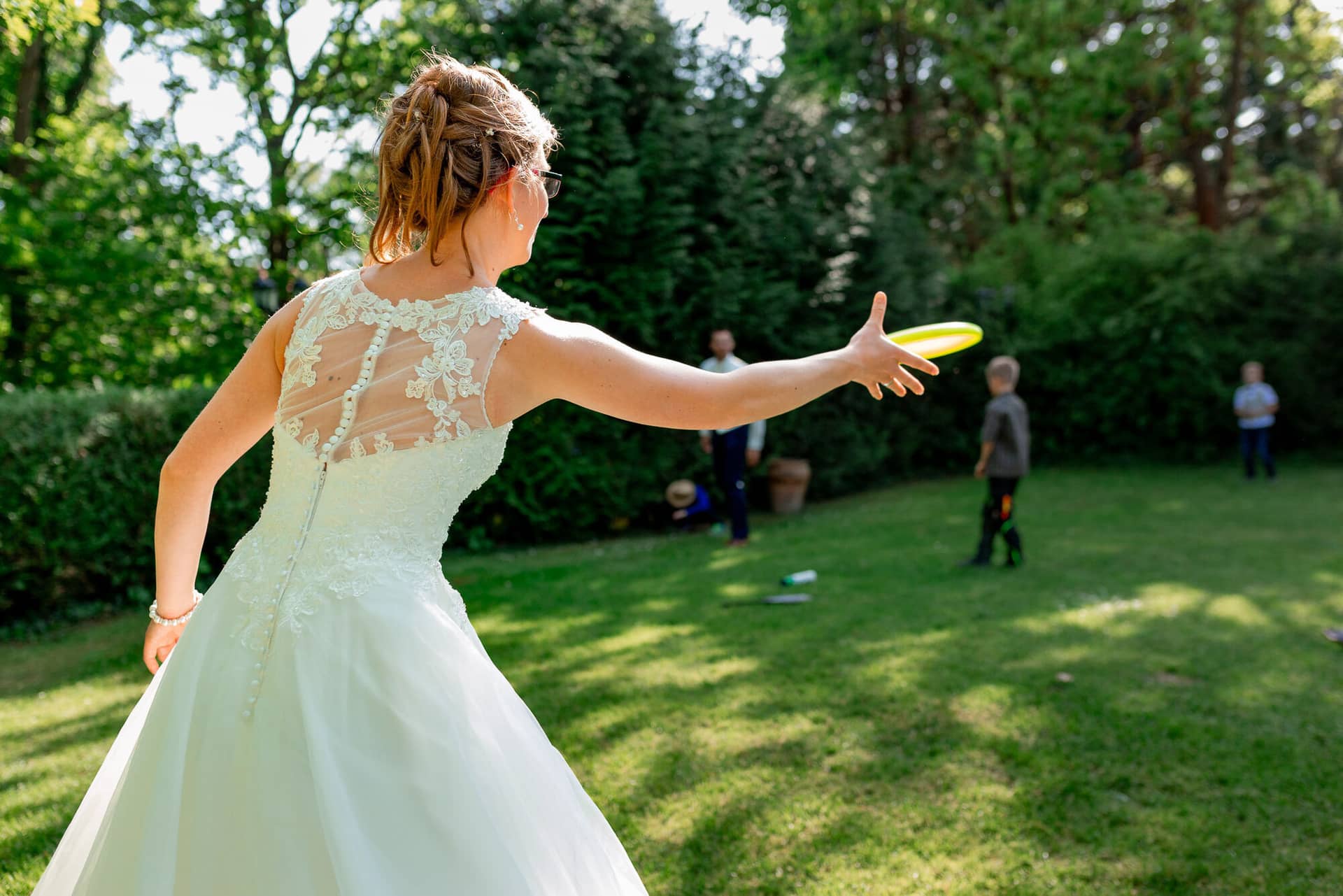 Anne Christian Hochzeitsfotograf Birkenheide Grosskarlbach Bissersheim 00029.BmVZtGkp Braut wirft ausgelassen einen Frisbee in den grünen Hochzeitsgarten im weißen floralen Kleid