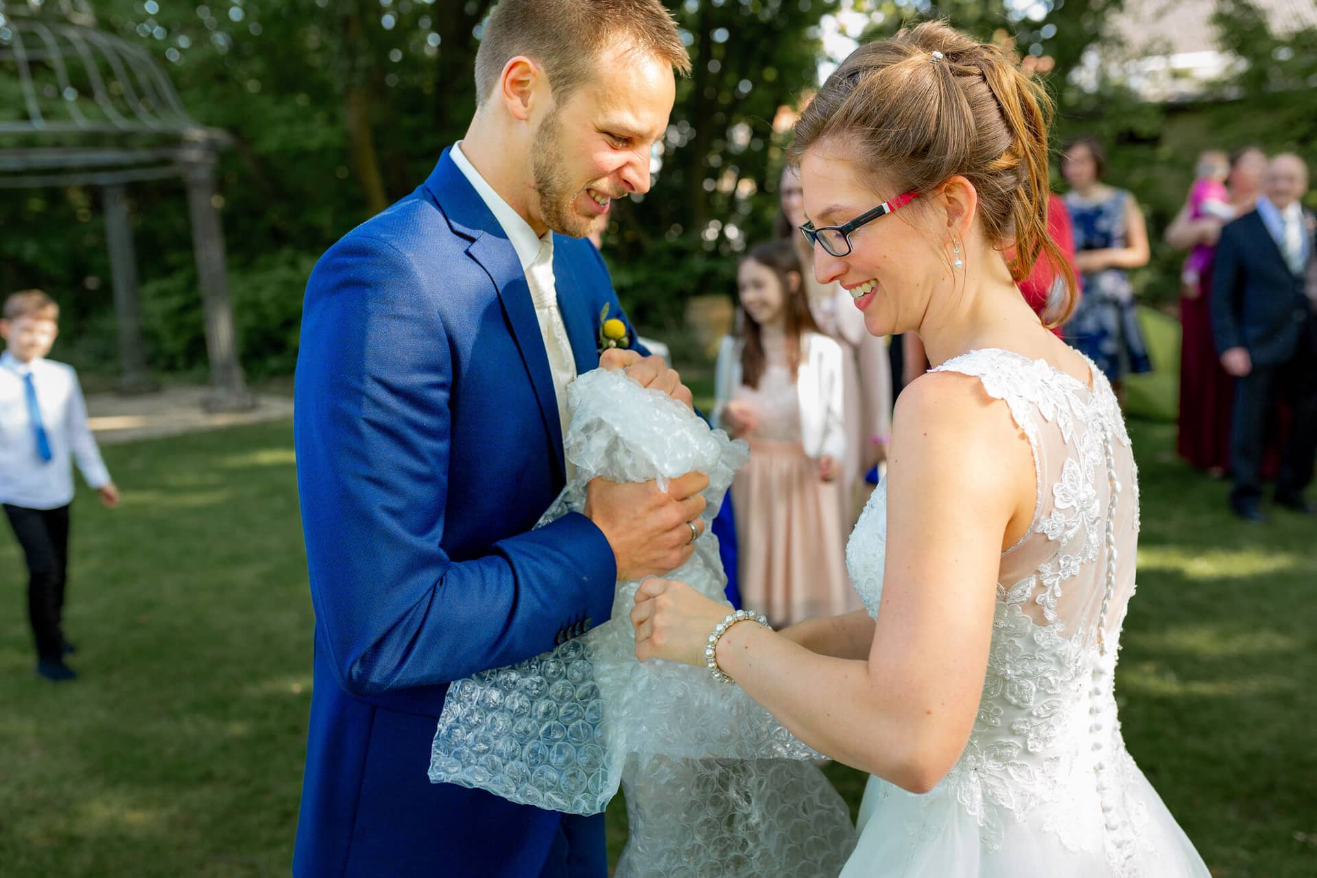 Anne Christian Hochzeitsfotograf Birkenheide Grosskarlbach Bissersheim 00030.BYad9 8V Bräutigam überreicht seiner lachenden Braut ein Seifenblasen-Set auf der grünen Wiese beim Sektempfang