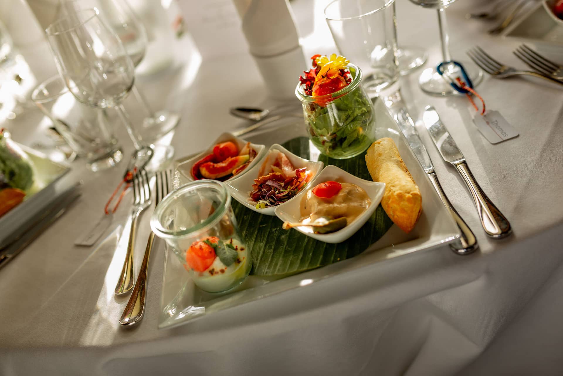 Anne Christian Hochzeitsfotograf Birkenheide Grosskarlbach Bissersheim 00032.D0cXCI9Z Tablett mit kleinen Vorspeisen – Salat, Garnelen, Dip und Brot – auf weißem Hochzeitstisch