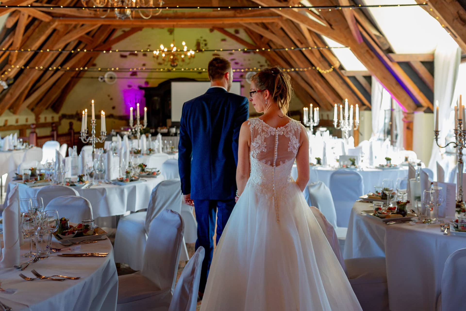 Anne Christian Hochzeitsfotograf Birkenheide Grosskarlbach Bissersheim 00036.CuLQBfeP Brautpaar schreitet gemeinsam durch prachtvollen Saal mit Kerzen und Festbeleuchtung