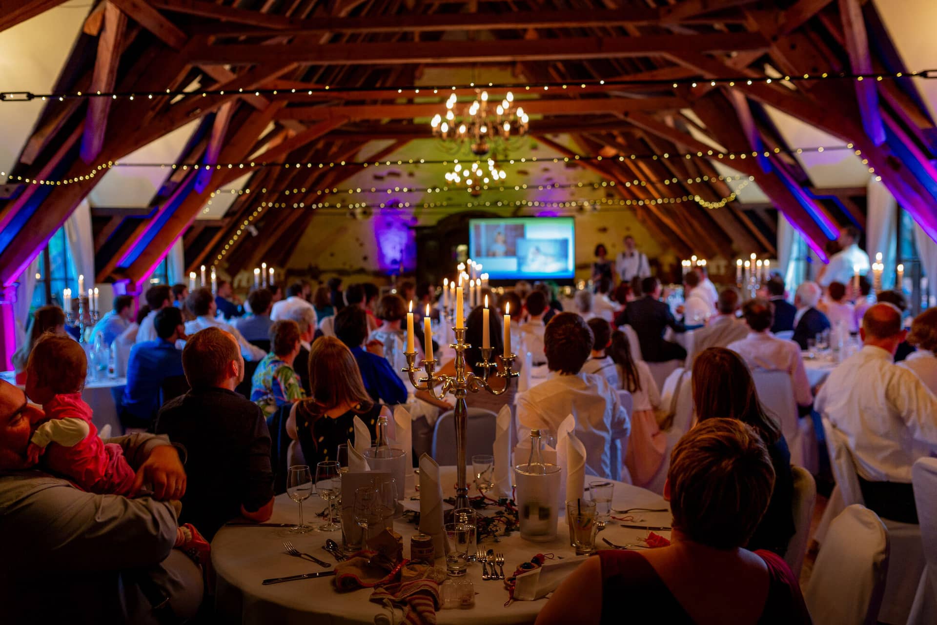 Anne Christian Hochzeitsfotograf Birkenheide Grosskarlbach Bissersheim 00037.Hgb546Eb Hochzeitsdinner in strohgedecktem Saal mit beleuchteten Tischen, Kerzen und vielen fröhlichen Gästen