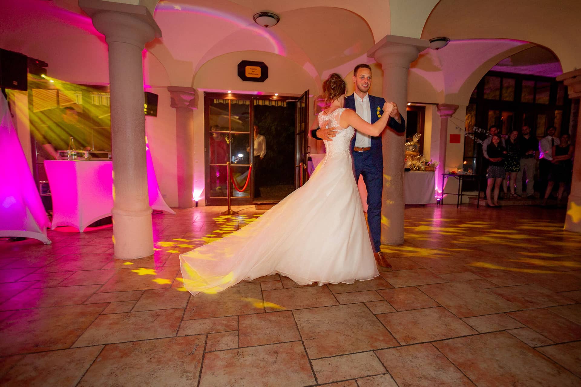 Anne Christian Hochzeitsfotograf Birkenheide Grosskarlbach Bissersheim 00041.DMJfXZl5 Brautpaar tanzt gemeinsam im rosa und gelben Scheinwerferlicht beim ersten Hochzeitstanz