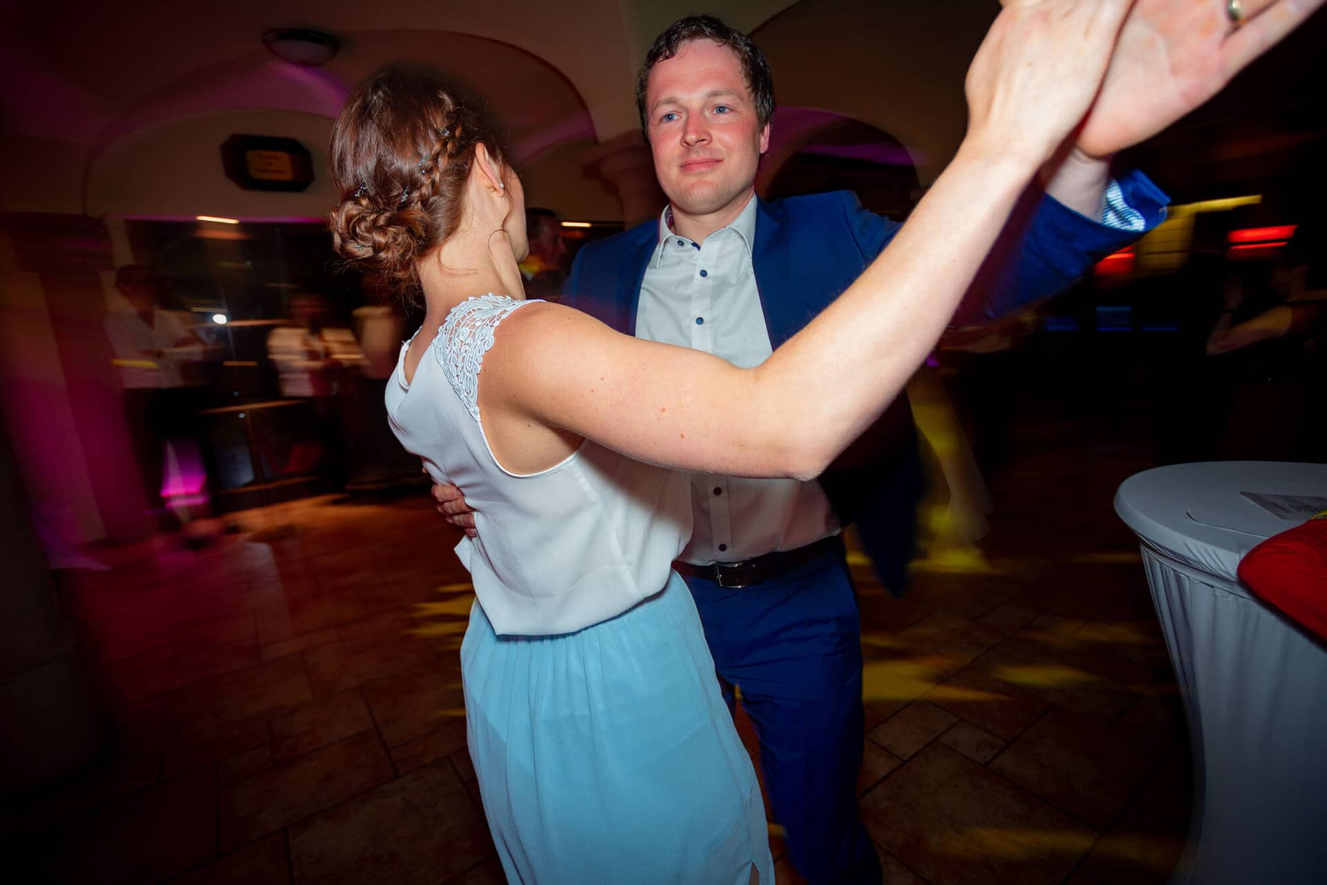 Anne Christian Hochzeitsfotograf Birkenheide Grosskarlbach Bissersheim 00042.BMei5Qql Brautpaar tanzt innig im Lichtschein der Hochzeitsparty, Mann hält die Hand seiner Partnerin