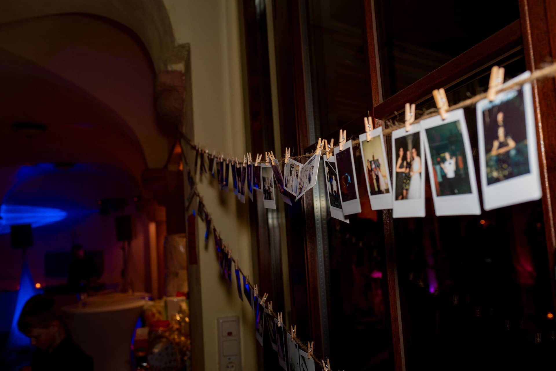 Anne Christian Hochzeitsfotograf Birkenheide Grosskarlbach Bissersheim 00046.DFLAPcY9 Girlande mit Polaroid-Hochzeitsfotos hängt dekorativ an dunklem Holzrahmen im festlich beleuchteten Saal