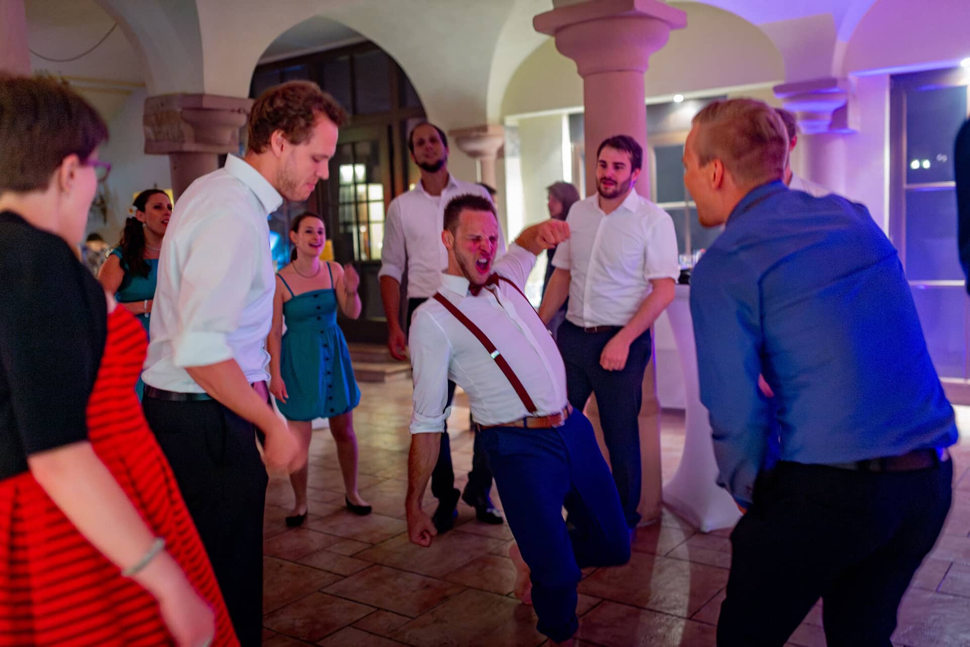 Anne Christian Hochzeitsfotograf Birkenheide Grosskarlbach Bissersheim 00052.BqlY3Mjs Gast tanzt ausgelassen mit anderen Feiernden in prächtigem Hochzeitssaal unter Kronleuchter