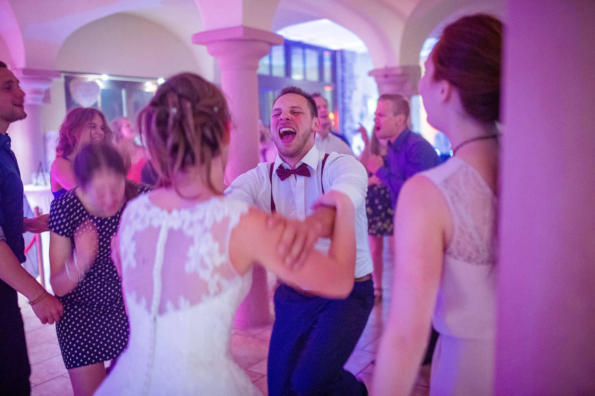 Anne Christian Hochzeitsfotograf Birkenheide Grosskarlbach Bissersheim 17.DopM6eik Jubelnder Bräutigam tanzt leidenschaftlich mit seiner Braut in rosa beleuchtetem Festsaal