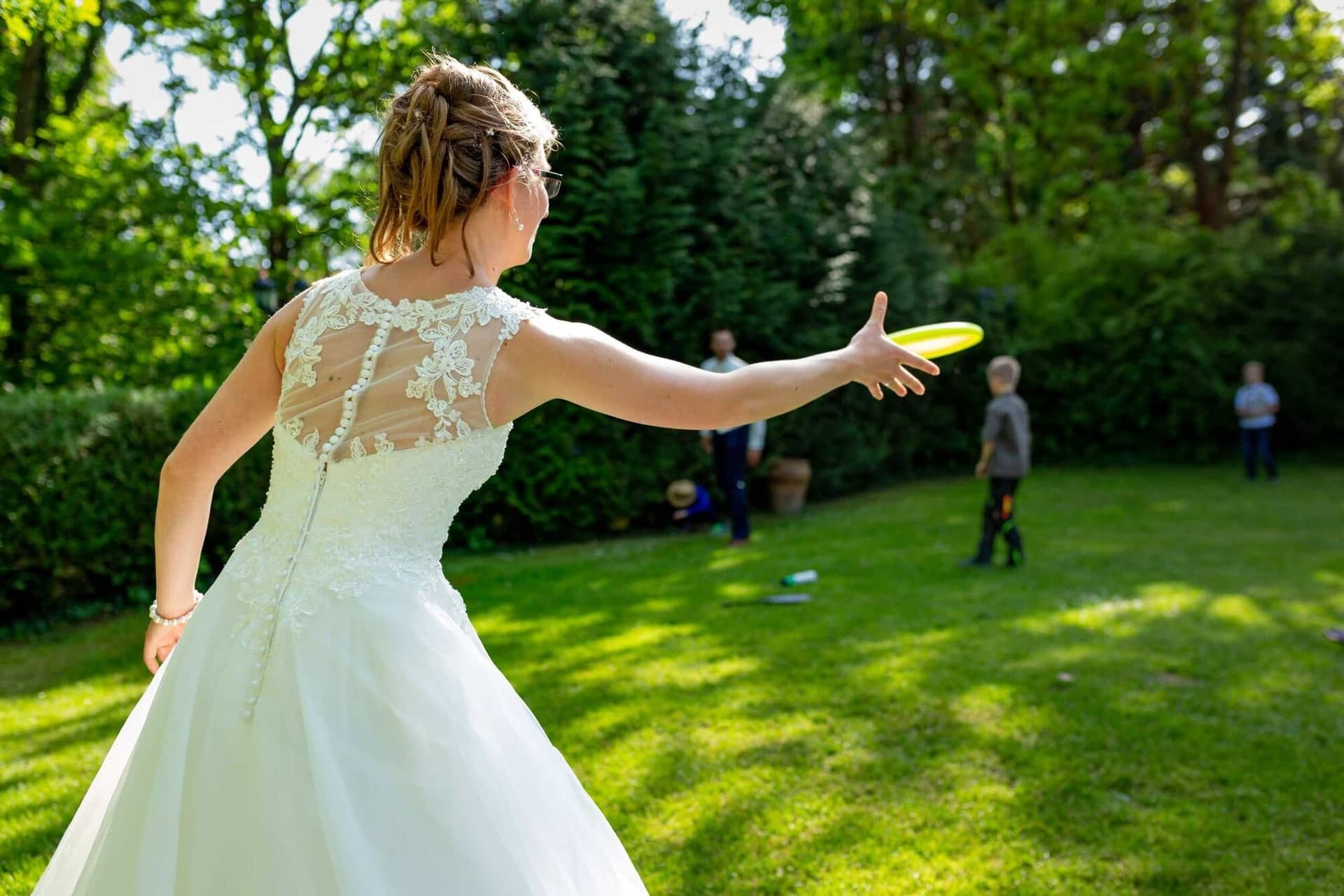 Anne Christian Hochzeitsfotograf Birkenheide Grosskarlbach Bissersheim 7.D4plx7qn Braut wirft einen Frisbee über die grüne Gartenwiese – ein entspannter Moment beim Hochzeitsempfang