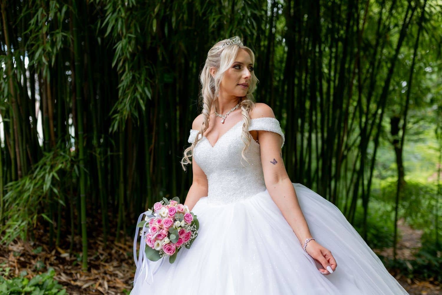 Brautpaarshooting Weinheim Schlossgarten Heidelberg Freie Trauung 4K8A5392 07b1c317 1500.DMXASENM Braut in glitzerndem weißem Ballkleid mit Blumenstrauß vor dichten Bambus-Pflanzen des Hermannshof-Gartens