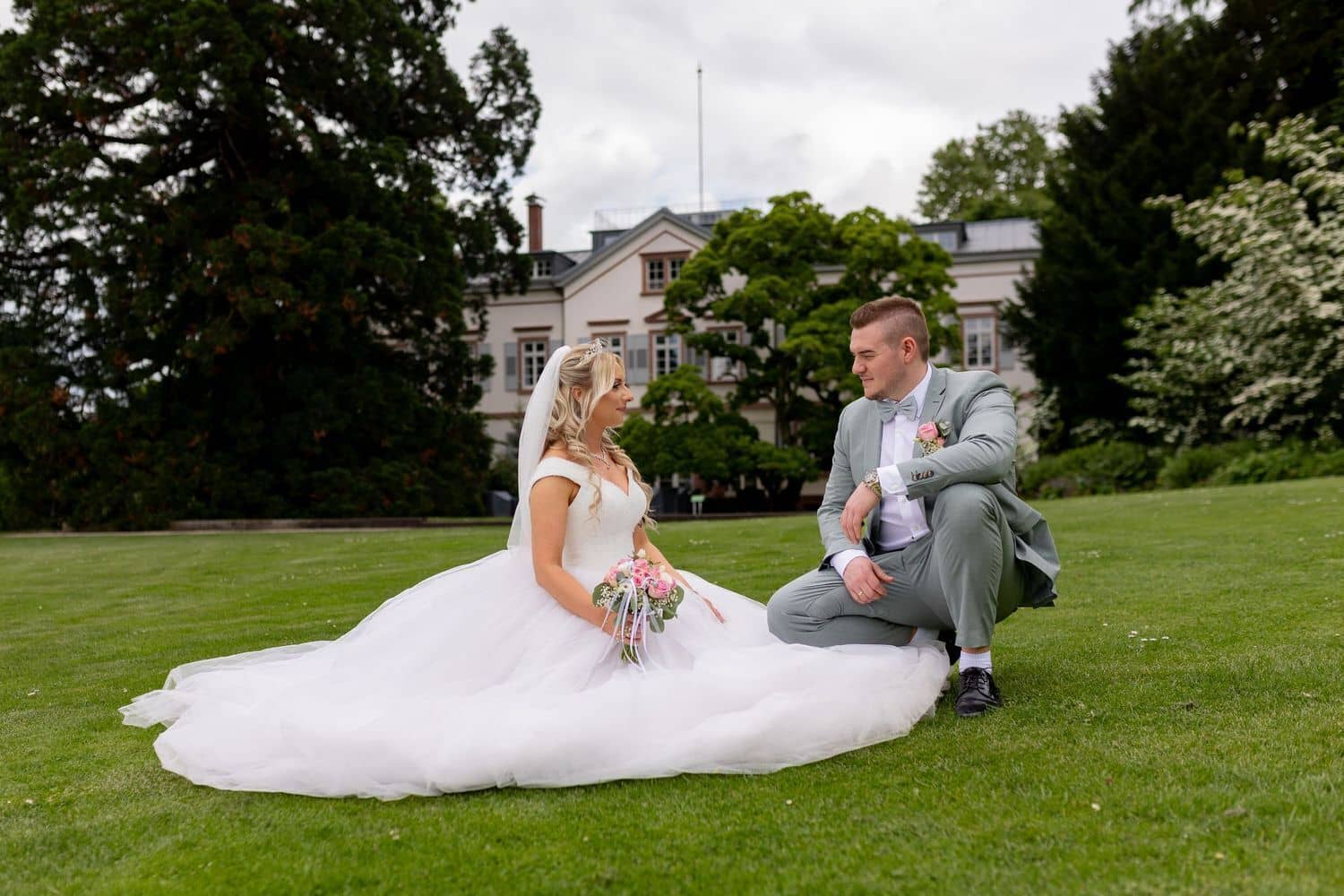 Brautpaarshooting Weinheim Schlossgarten Heidelberg Freie Trauung 4K8A5853 898748fa 1500.GOD5mX5X Brautpaar sitzt auf der Wiese und unterhält sich, historisches Herrenhaus des Hermannshofs im Hintergrund