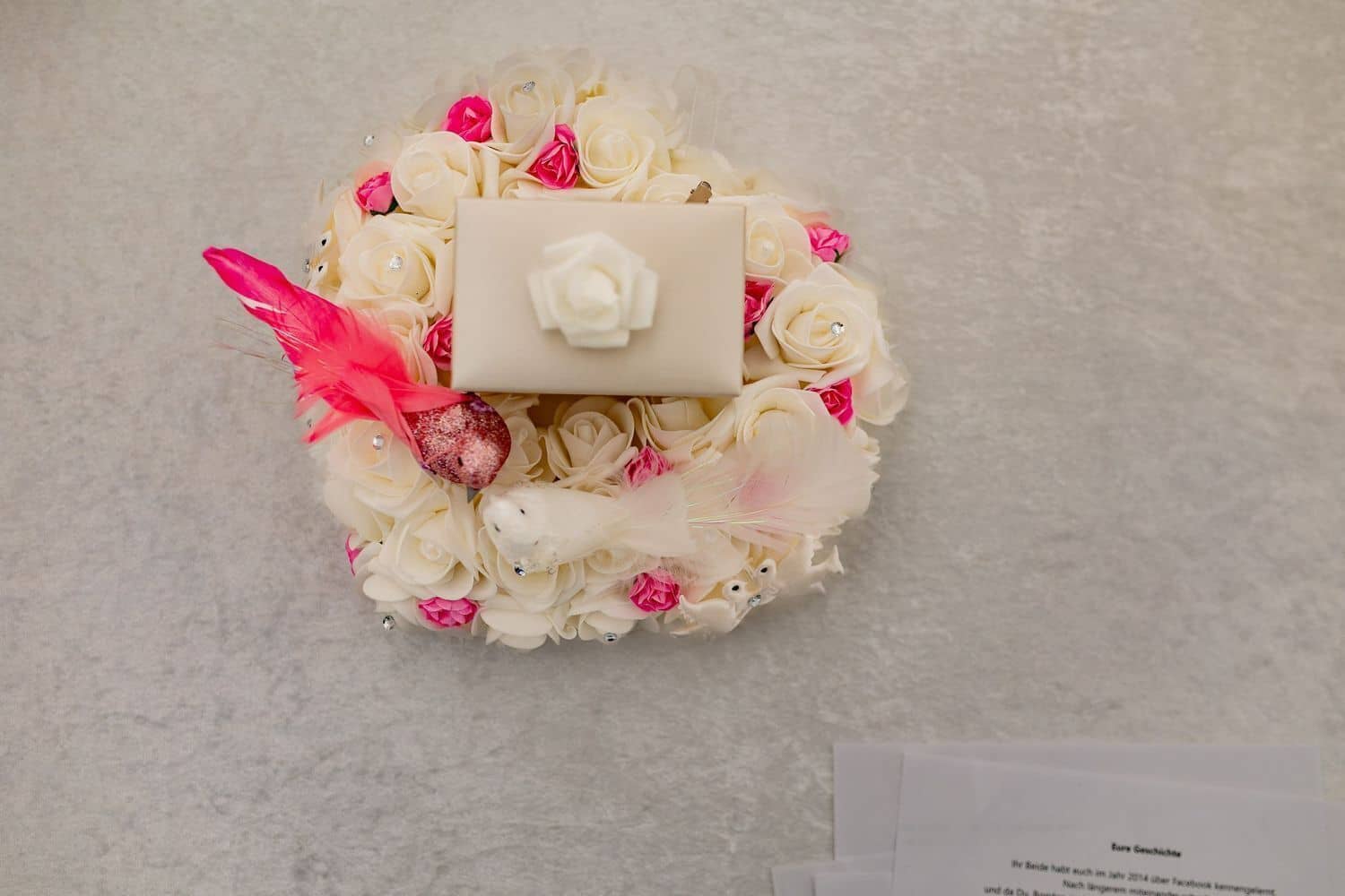 Brautpaarshooting Weinheim Schlossgarten Heidelberg Freie Trauung 4K8A6041 540bcf86 1500.ByKQbJvd Detailaufnahme des weißen Ringkastens mit weißen Rosen, Kristallen und einer roten Feder