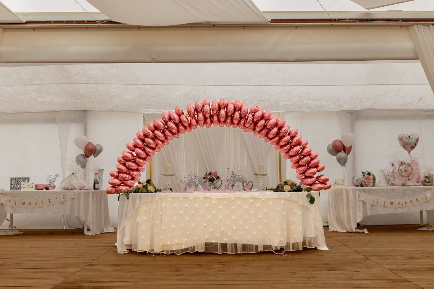 Brautpaarshooting Weinheim Schlossgarten Heidelberg Freie Trauung 4K8A7851 45f28645 1500.BbgWOfUd Großer rosa-goldener Luftballonbogen über dem Deko-Tisch, Gäste im weißen Festzelt dahinter