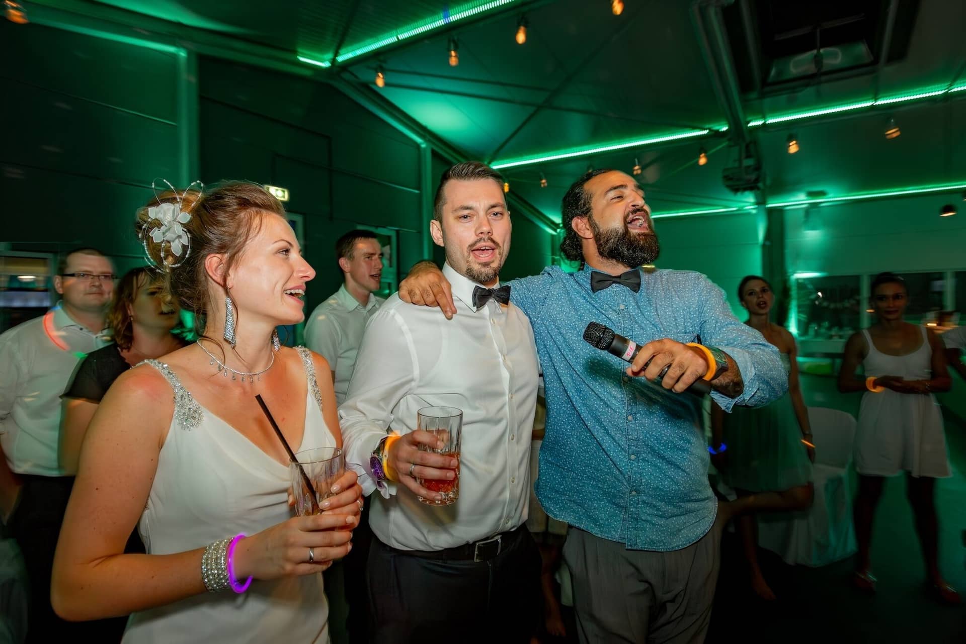 Hochzeit Schwetzingen Hochzeitsfotograf Heiraten Miio MK3 9510 Verbessert RR.DBEzpTaA Bräutigam singt leidenschaftlich ins Mikrofon, umgeben von Braut und jubelnden Gästen bei grüner Party-Beleuchtung