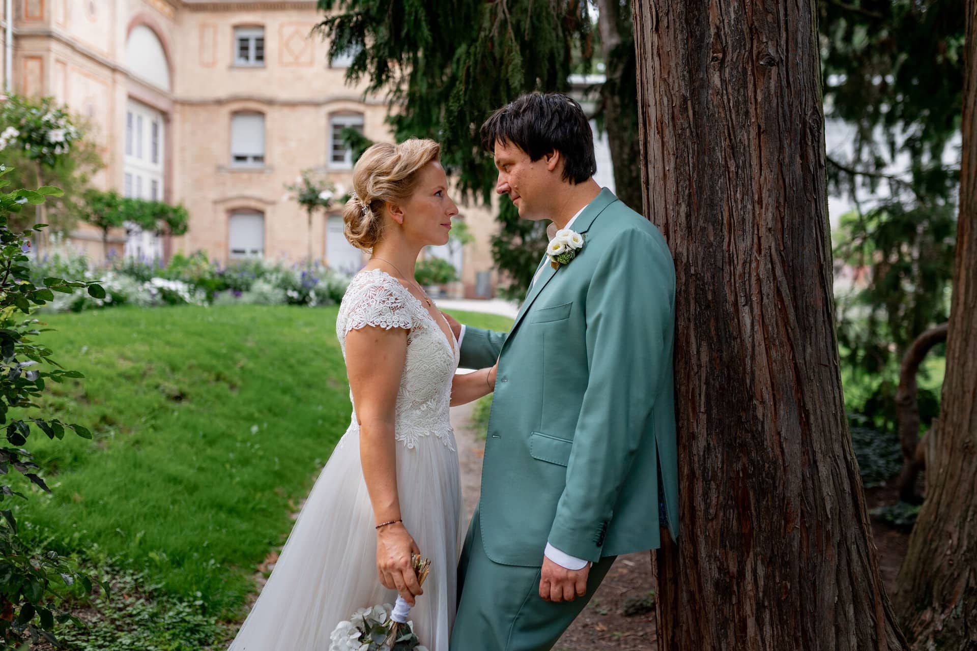 Hochzeitsfotograf Karlsruhe Daniela Matthias 20230819 14 15 38 4K8A5352.CsZA4 LE Brautpaar steht sich auf einem Gartenweg gegenüber und schaut sich liebevoll an, alter Baum und Gartenanlage im Hintergrund