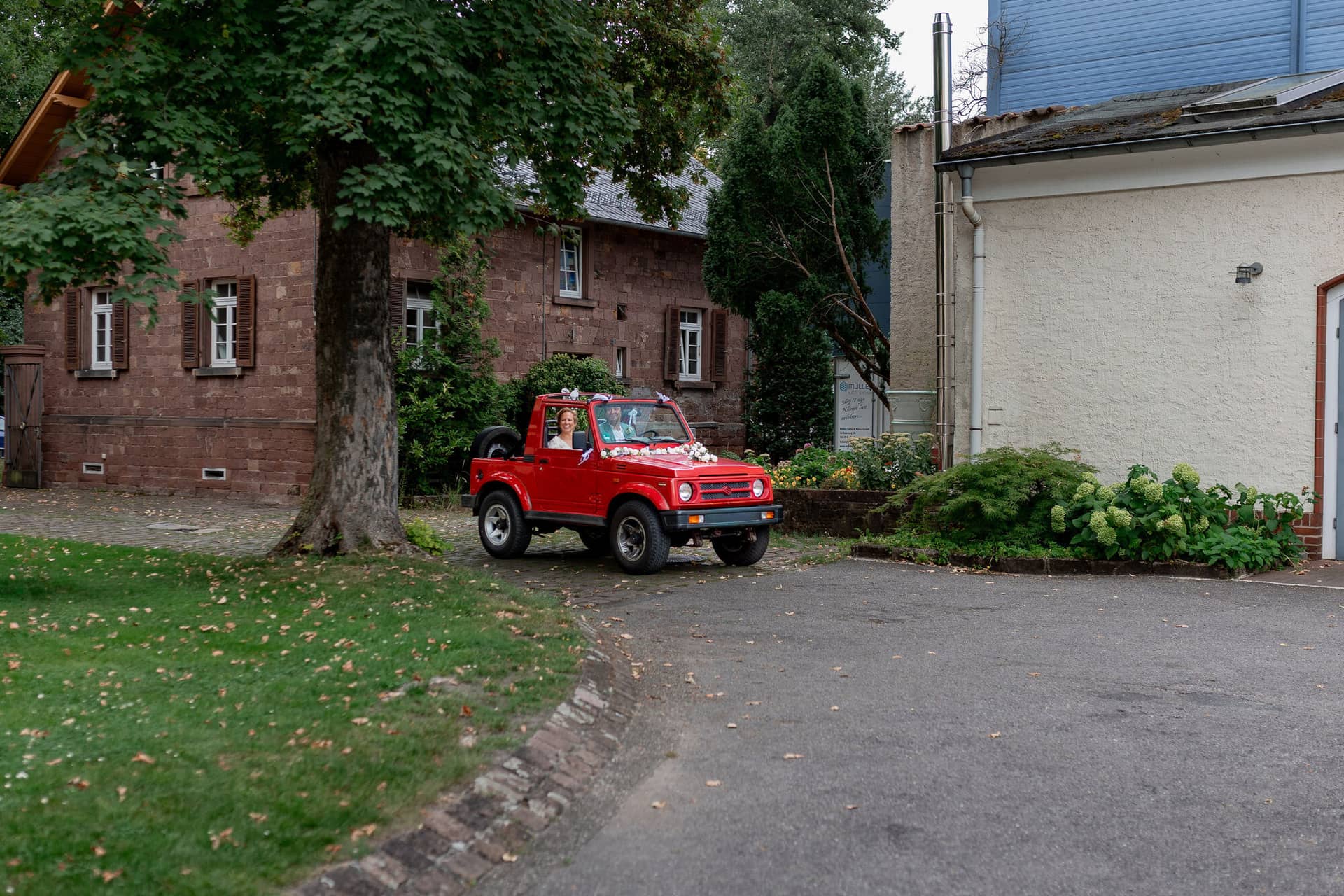 Hochzeitsfotograf Karlsruhe Daniela Matthias 20230819 15 20 06 4K8A6656.CgbDt4v4 Rotes Geländefahrzeug mit Brautpaar und Blumenkorb vor Backsteingebäude der Majolika Manufaktur Karlsruhe
